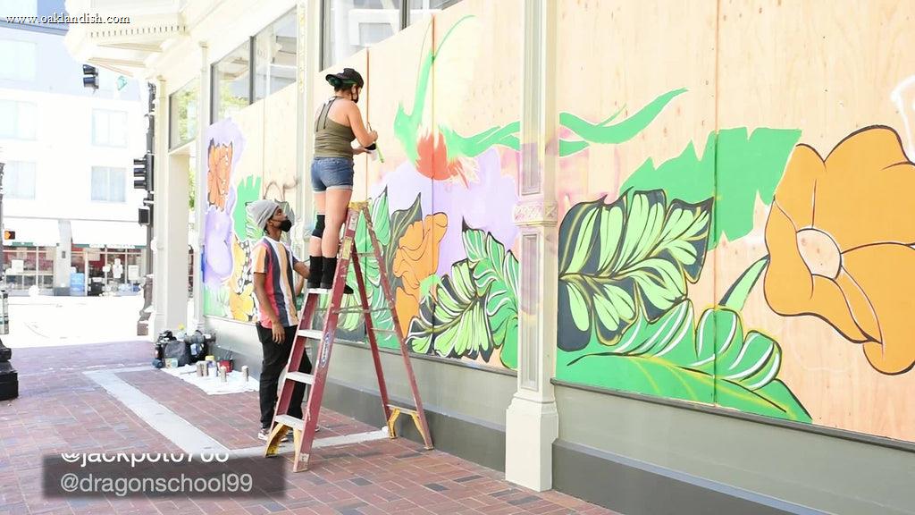 two people, one on ladder, painting a mural on the side of a building