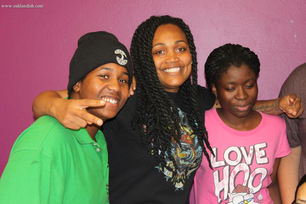 three smiling people, pink wall, one wearing a black Oaklandish beanie