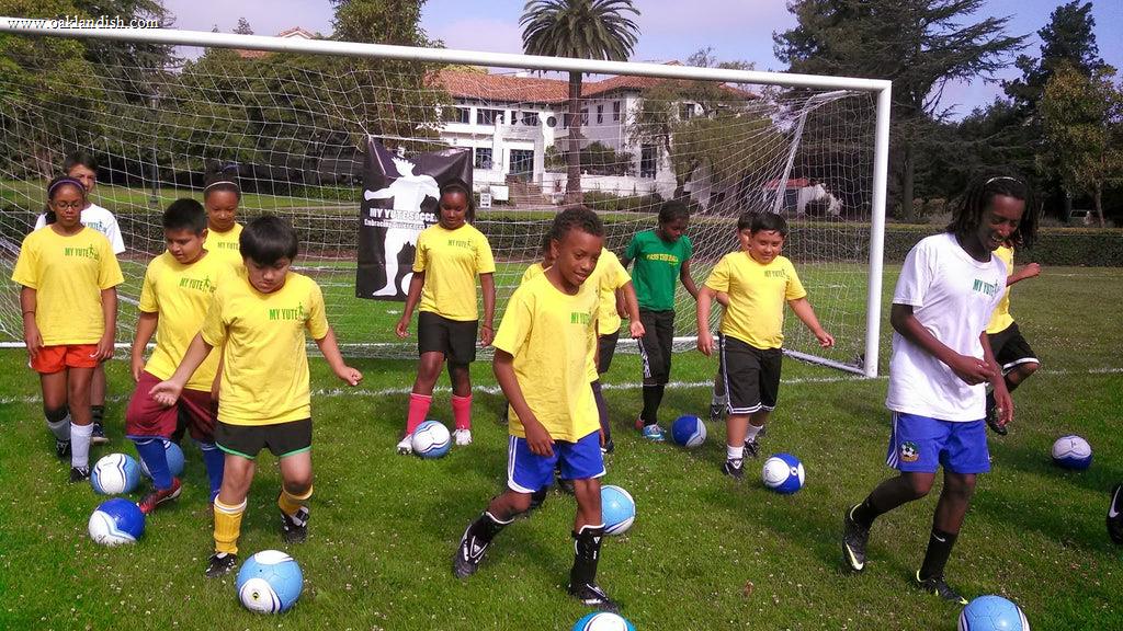 kids playing soccer in front of a goal on an outdoor grass field