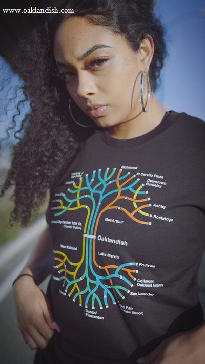 Woman standing under an overpass wearing a black t-shirt with a BART transit map in the shape of the Oaklandish tree logo.