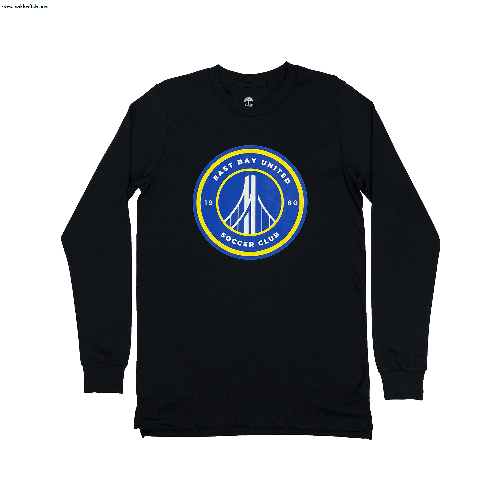 The EBU Long Sleeve Tee by Supported Brands is a black shirt with long sleeves, featuring a circular emblem prominently displayed on the front center. The emblem showcases a blue background with a white bridge illustration at its core, encircled by a yellow border. Surrounding the bridge design, the text "East Bay United Soccer Club" and "1980" are finely written in white letters, celebrating the storied youth soccer club.