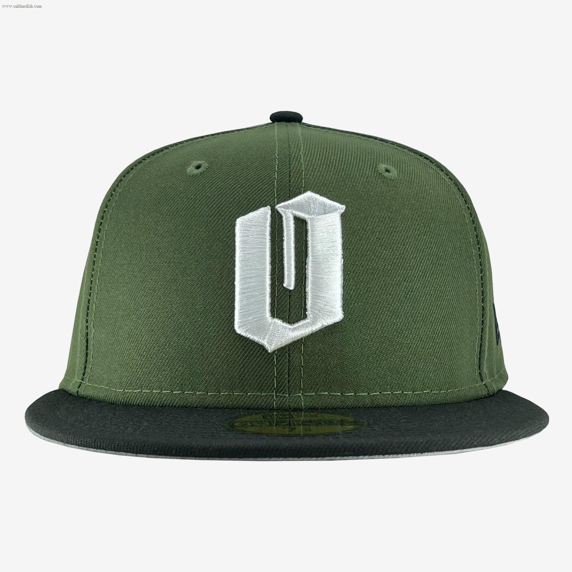 A New Era Official 59FIFTY Fitted Cap by Other, this green snapback features a bold, white embroidered “U” in a stylized font on the front panel and a black flat brim. Inspired by classic fitted cap design, it adds an Oaklandish edge to your style. The plain white background emphasizes the cap’s color and distinctive details.
