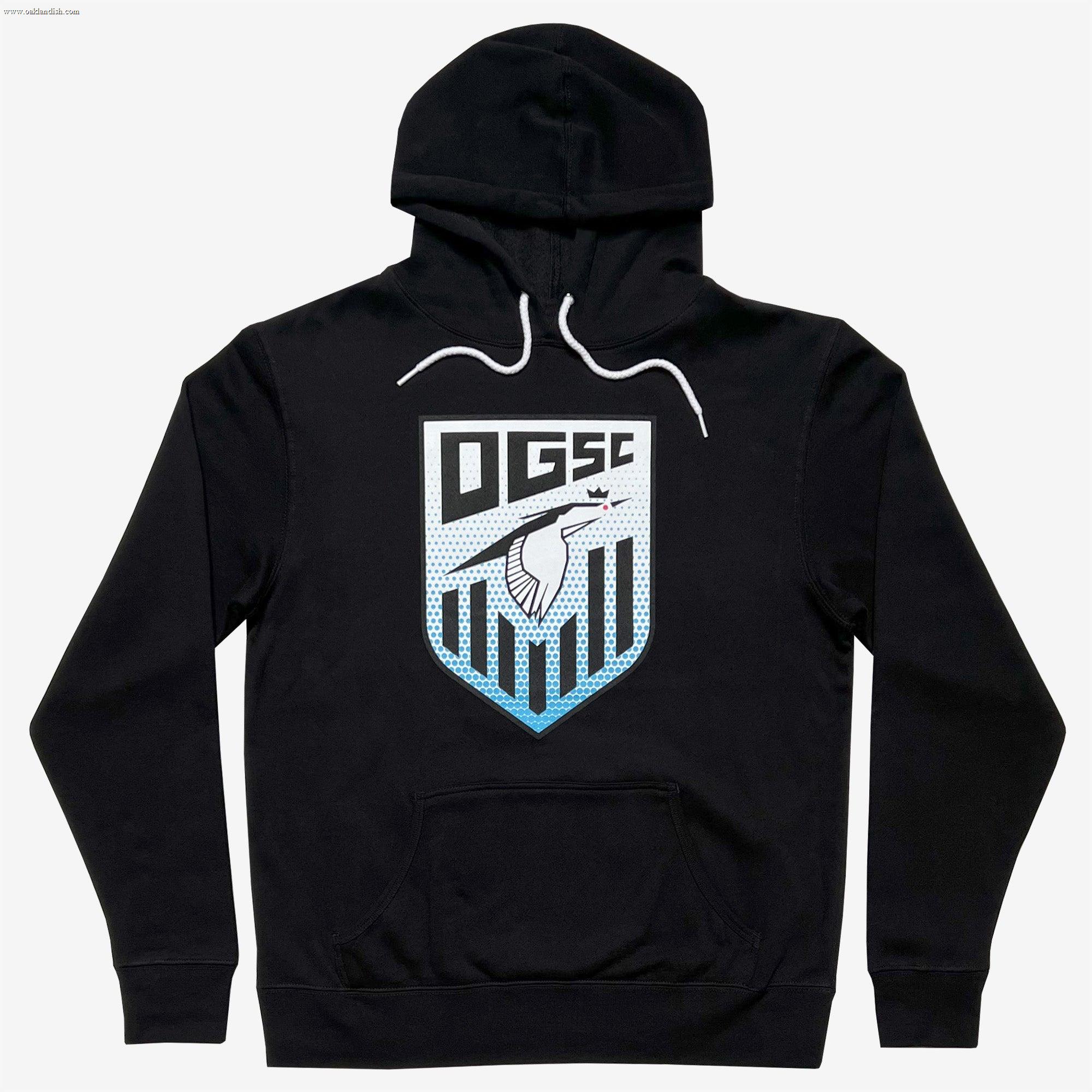 The Oakland Genesis Heron Hoodie by Partner is a black hooded sweatshirt with a front pocket, featuring a bold chest design that includes the letters "OGSC" above a stylized shield representing Oakland Genesis youth soccer. This eye-catching graphic also showcases a bird in white and blue tones against a dotted background, finished with white drawstrings at the neck.