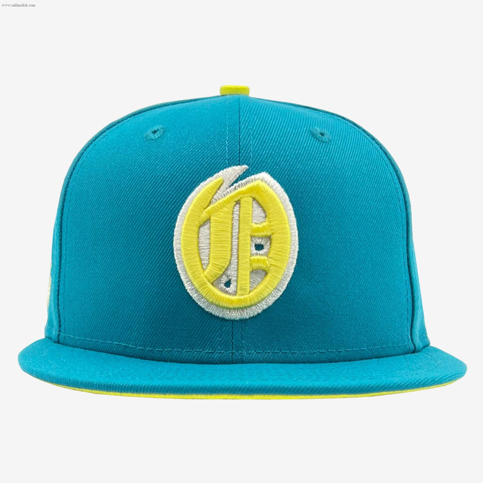 A turquoise New Era Oakland Oaks 59FIFTY fitted cap featuring a bold, circular yellow and white embroidered logo with stylized overlapping letters on the front. This Other brand hat includes yellow accents along the brim’s edge and a matching button on top, set against a plain white background.