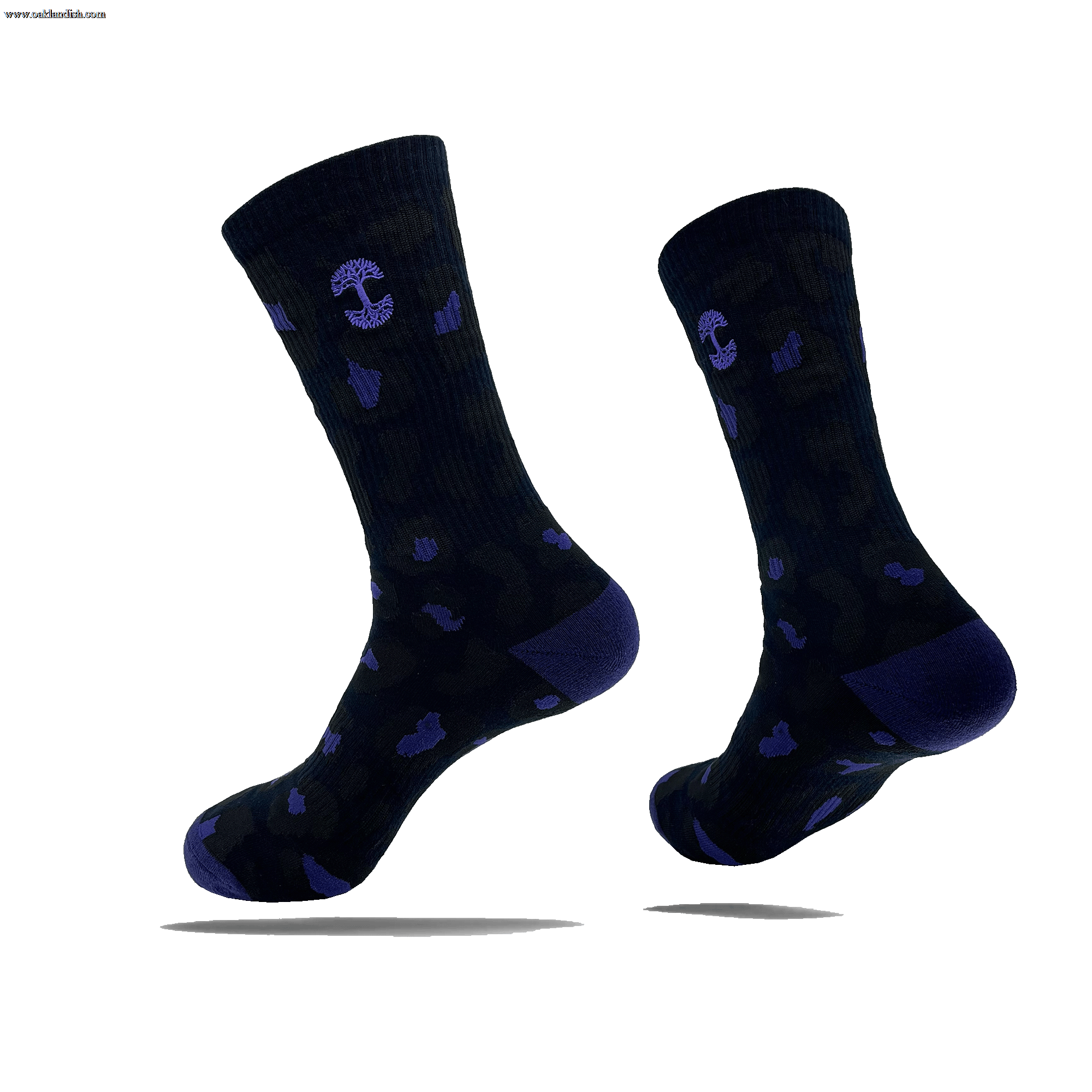 Introducing the Oaklandish Panther Sock: a versatile pair of black crew socks adorned with a subtle camouflage pattern, featuring small purple accents and anchor symbols. These mid-calf length socks come with dark heel and toe sections, creating an illusion of floating in mid-air when displayed against a light background. Designed as one size fits most for versatile wear.