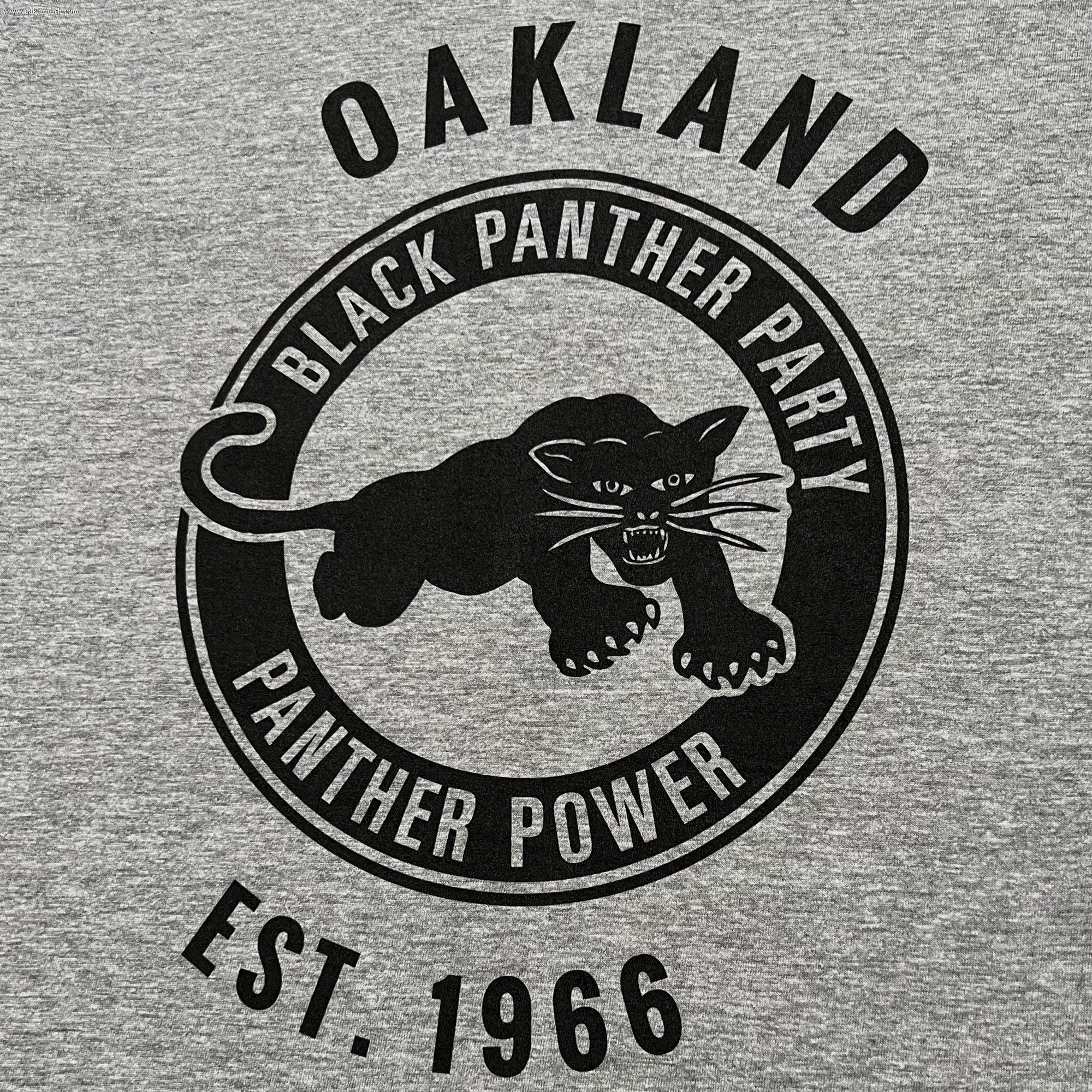The Black Panther Power Tee by Oaklandish features a black design on a gray t-shirt with a central image of a panther in a pouncing position. The text "BLACK PANTHER PARTY" encircles the top of the panther, while "PANTHER POWER" is at the bottom. Above and below this circular design, additional text celebrates the influential community organization with "OAKLAND" and "EST. 1966.
