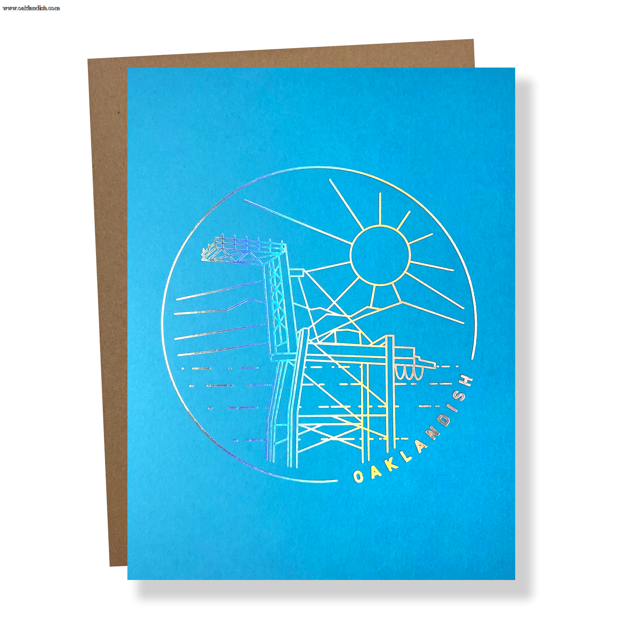 Blue greeting card with a circular gold line drawing of an Oakland crane and OAKLANDISH wordmark with a brown envelope.