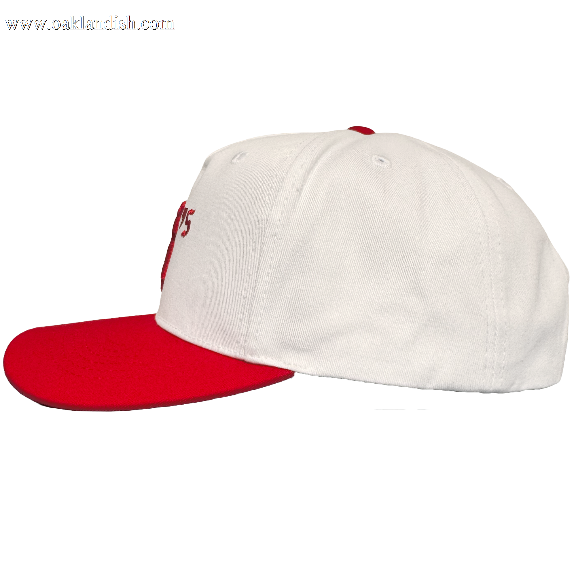 The Oakland Ballers 5 Panel Cap by Oakland Ballers is a white snapback hat with a flat red brim and button, side view. It has white panels, vent holes, visible stitching, and partial red embroidered "Oakland Ballers" text on the front. Plain white background.