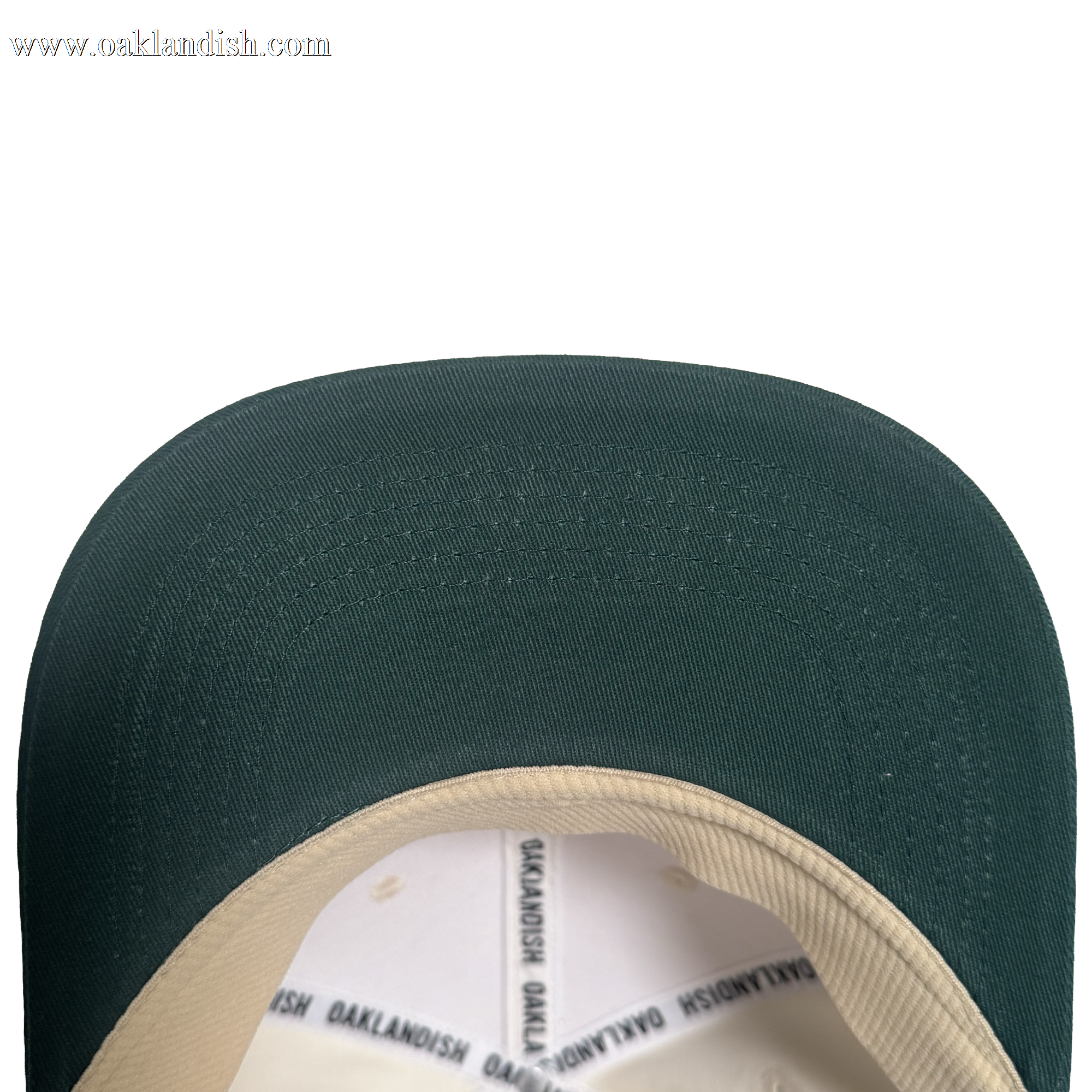 Close-up view of the brim and part of the inner lining of the Oakland Peloteros Hat by Oakland Ballers. The hat features a green brim and a beige inner lining with repeating black "OAKLANDISH" text. Set against a plain white background, only the top portion of this classic design is visible—a stylish nod to Oakland baseball team pride.