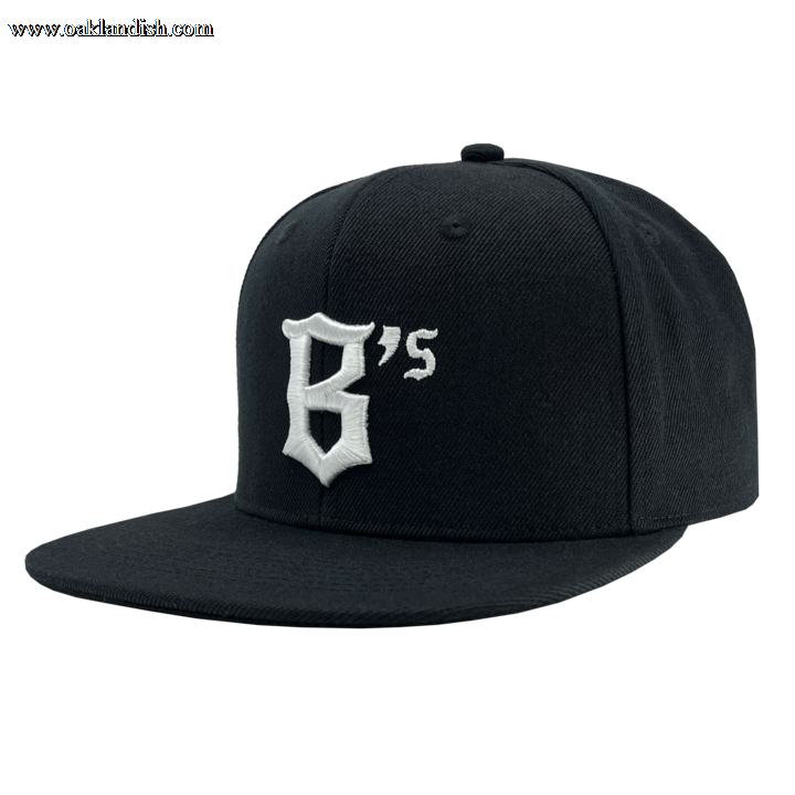 The Oakland Ballers Snapback is a black flat-brim baseball cap featuring an embroidered design on the front panel. The design showcases the character "B" with a small "s" beside it in white thread, styled in an angular, gothic font. Inspired by the spirit of the Oakland Ballers, this cap boasts a classic six-panel structure and a top button.