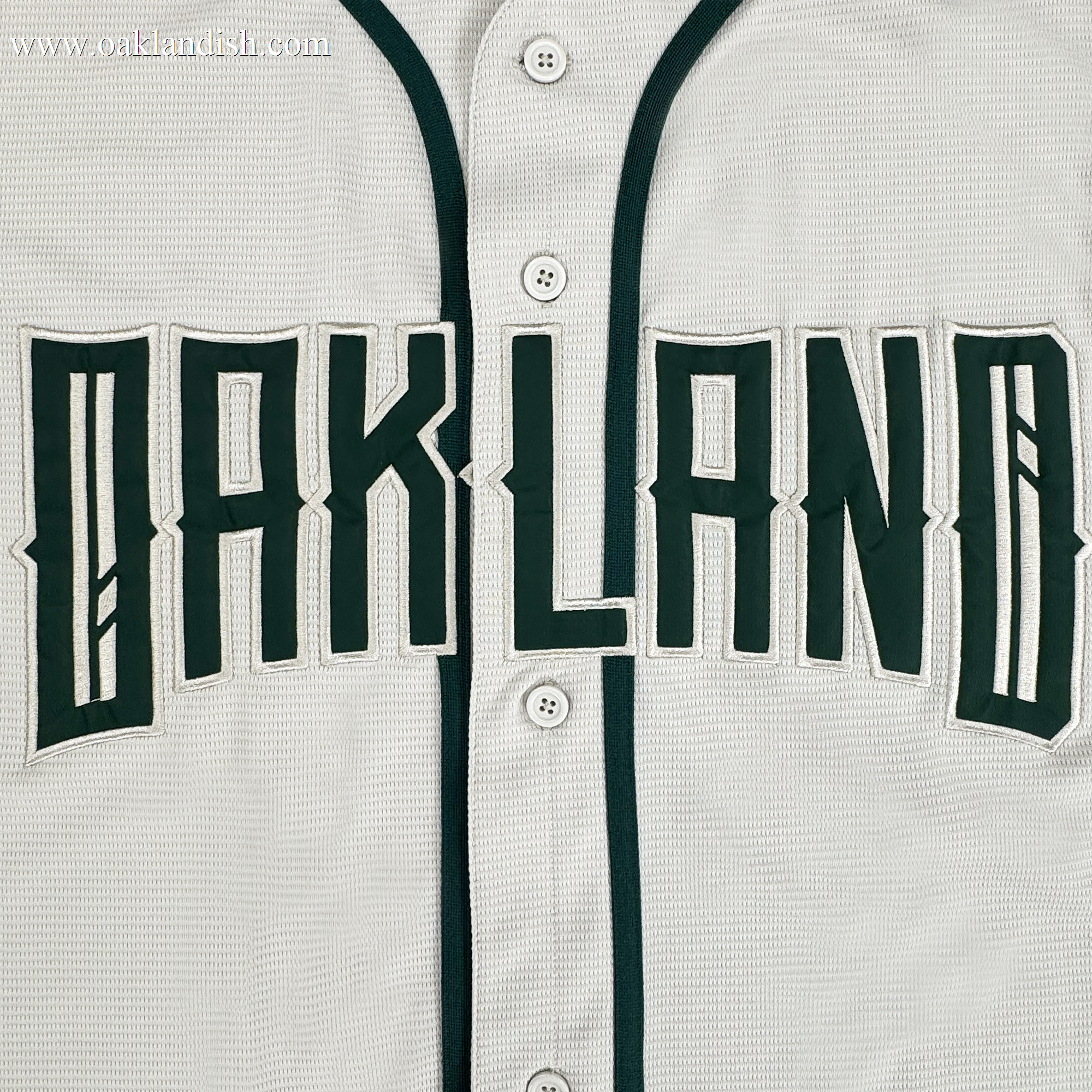 A close-up of the Oakland Ballers Button Up Jersey, featuring white fabric with dark green trim and buttons. “OAKLAND” is boldly displayed across the chest, representing the Oakland Ballers brand.