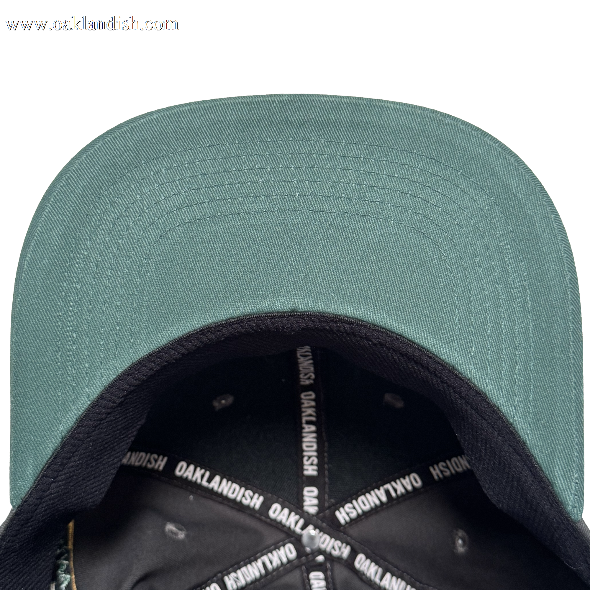 A top-down view of the Oakland Ballers Logo Hat by Oakland Ballers shows the green cap with black brim, white “OAKLANDISH” text on the inner band, and metal rivets around the crown, celebrating the Oakland baseball team.