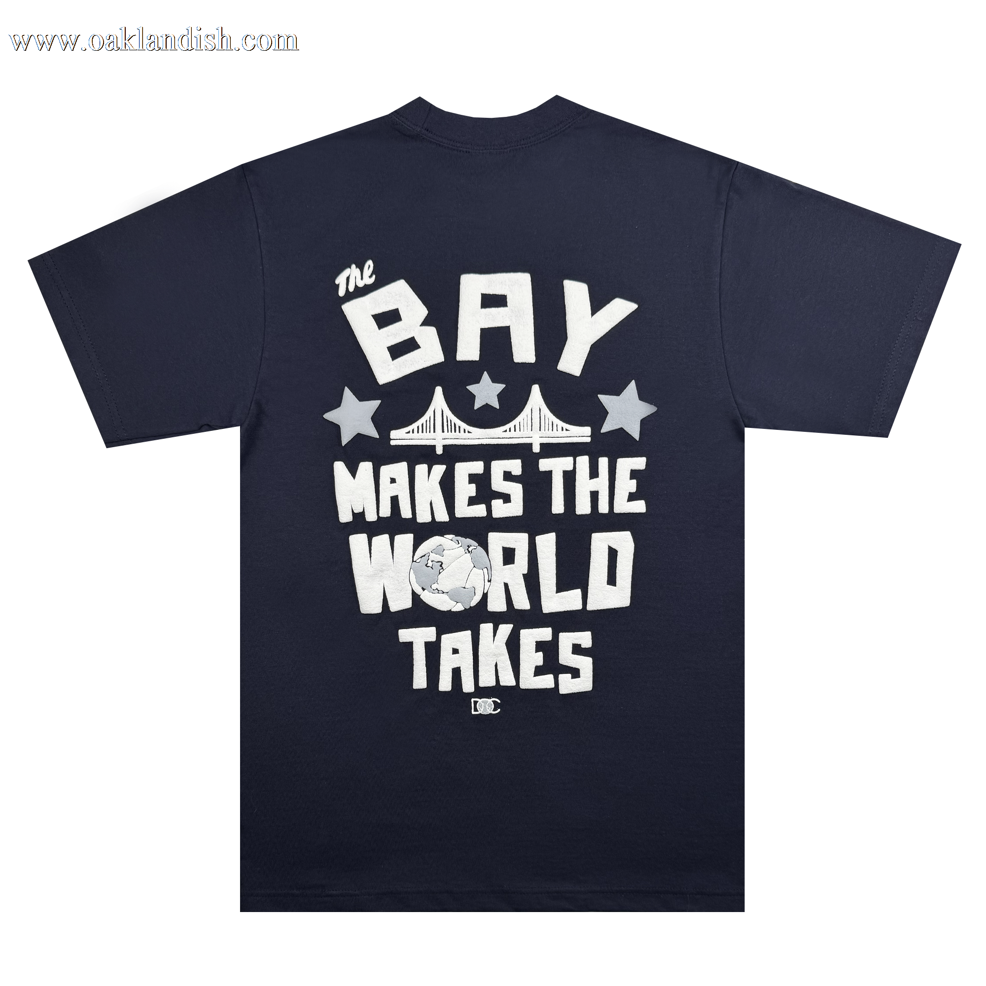 The Bay Bridge Tee by DOC from Oaklandish features a navy blue T-shirt with bold white text, "The Bay Makes The World Takes," encircling a bridge, stars, and globe, merging urban and global culture to highlight the Bay Area's worldwide artistic influence.