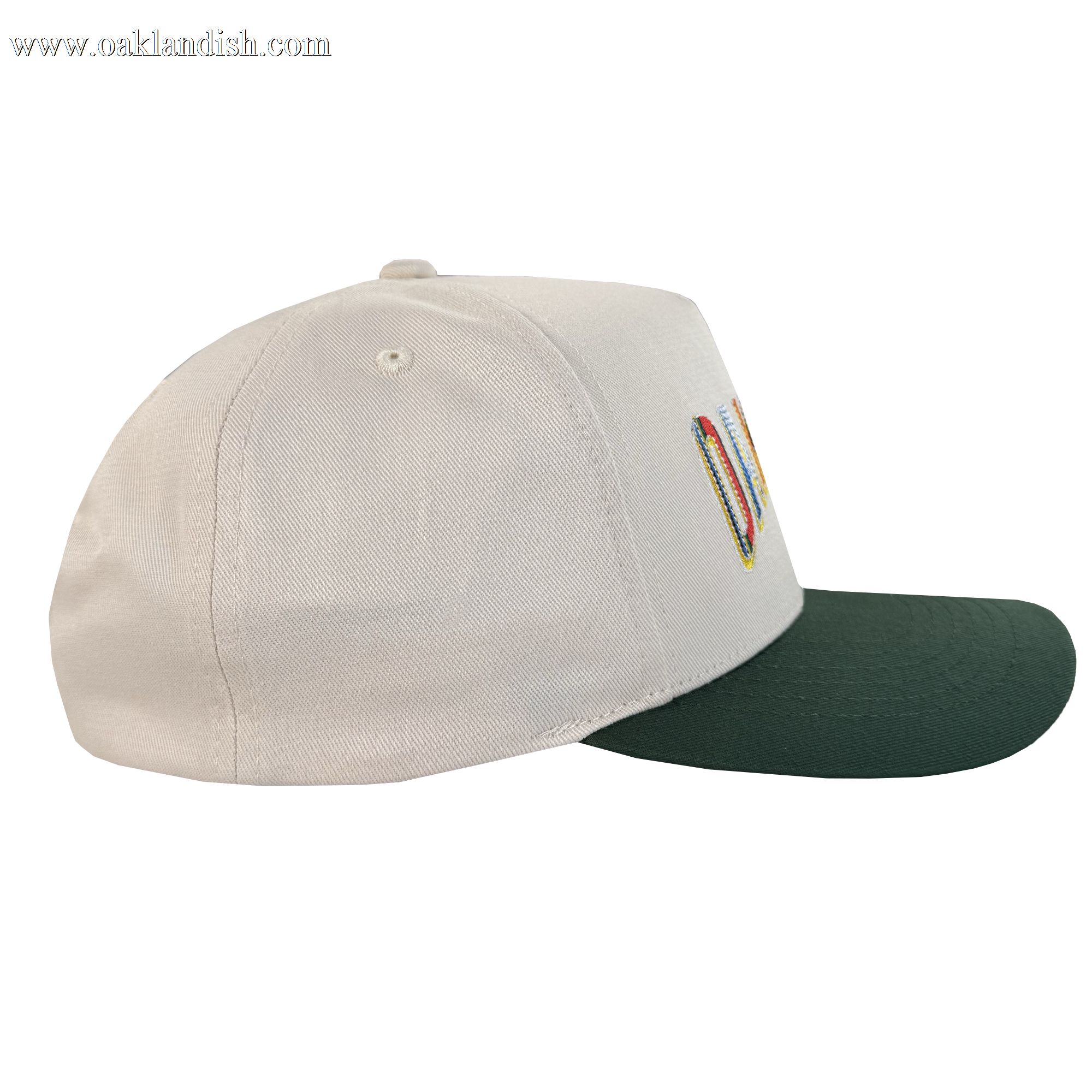 The Oakland Ballers Oakland Beisbol 5 Panel Cap is a beige snapback with a dark green curved brim, stitched eyelets, and part of a colorful embroidered front design visible from the side.