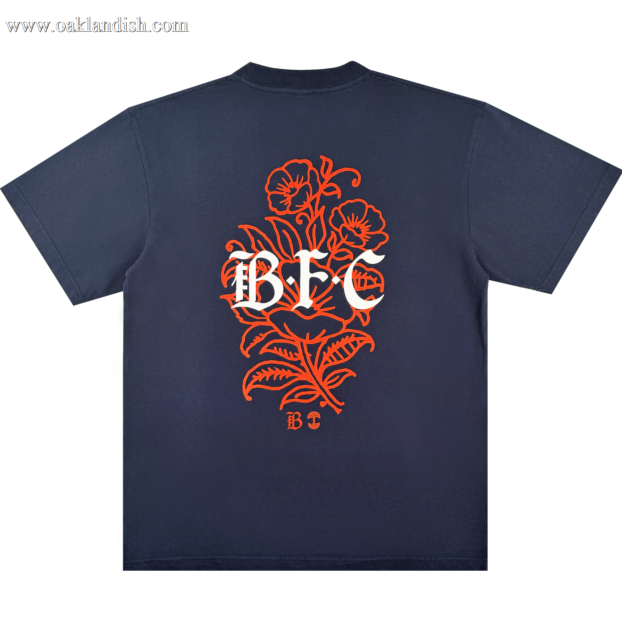 The Bay FC Flora Tee by Bay FC is a navy blue, classic fit shirt made from heavy-weight cotton. The back displays a large orange floral design with bold white "BFC" lettering and a small "BFC" below, celebrating Bay FC style.