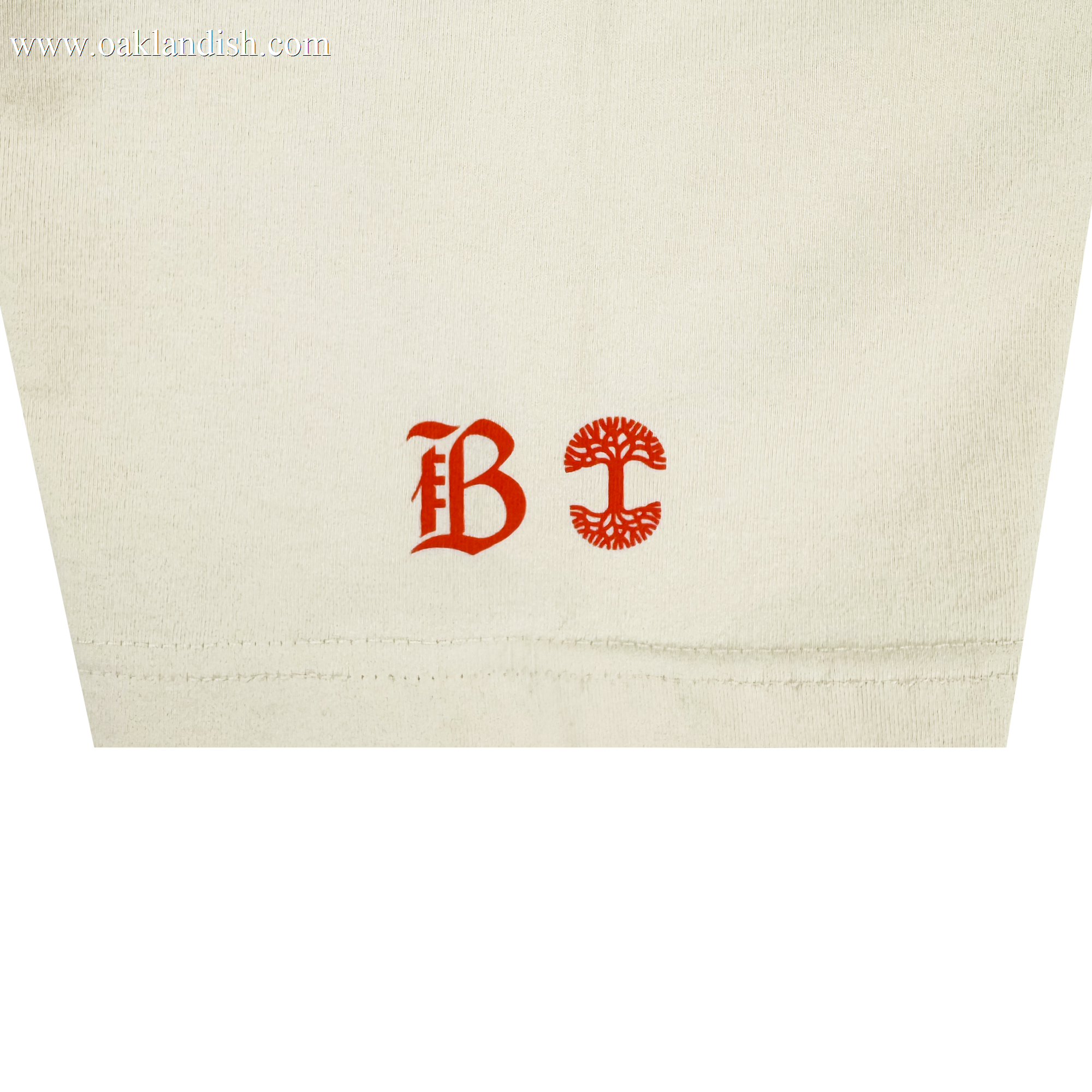 Close-up of heavy-weight cotton on the Bay FC Jubilee Tee: near the hem are two red symbols—a Gothic "B" on the left and a circular, tree-like emblem on the right.