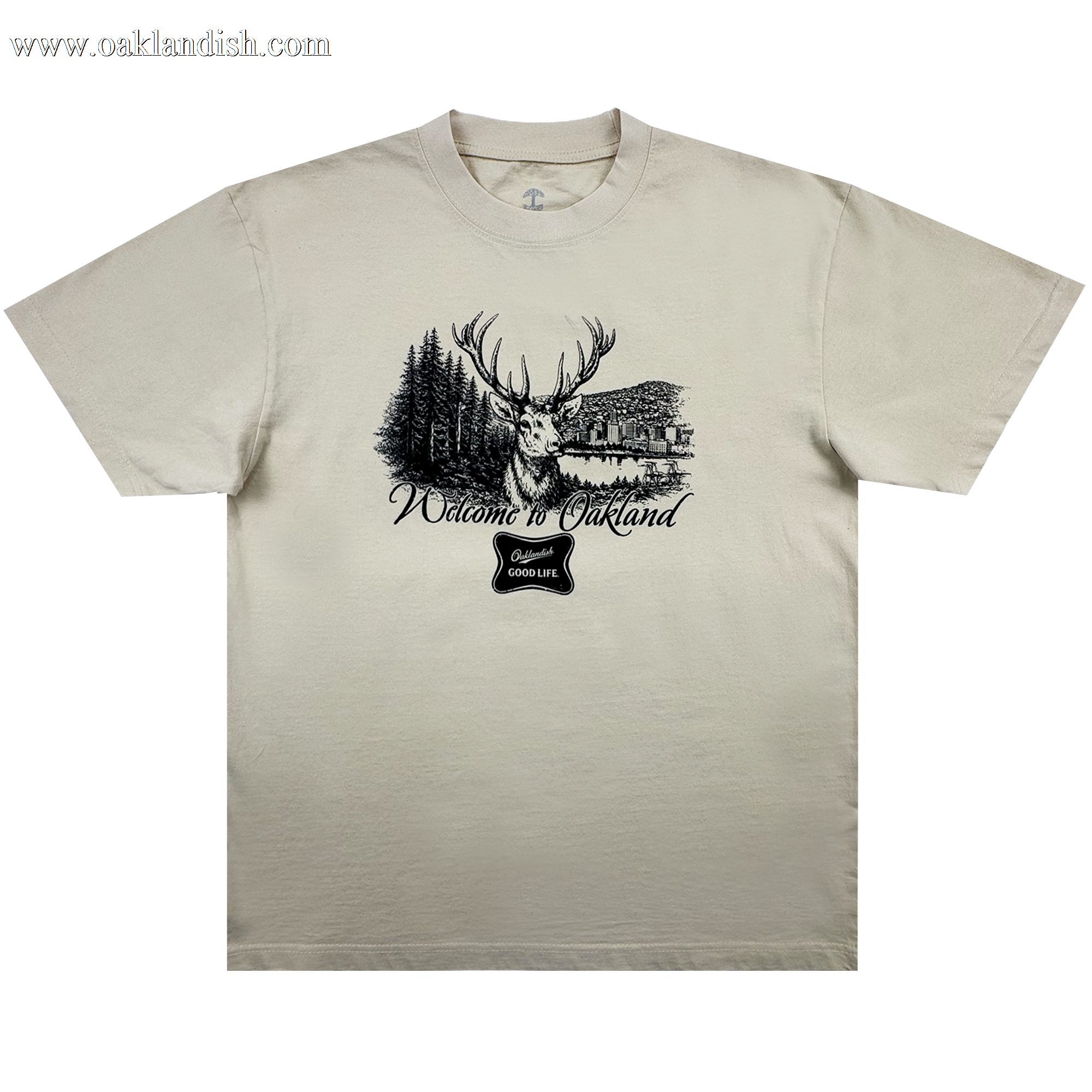The Buck Tee by Oaklandish is a beige men’s t-shirt with a black stag, pine trees, and lake cabin graphic. Made from heavy-weight cotton, it features "Welcome to Oakland" in cursive and a “good life” badge below.