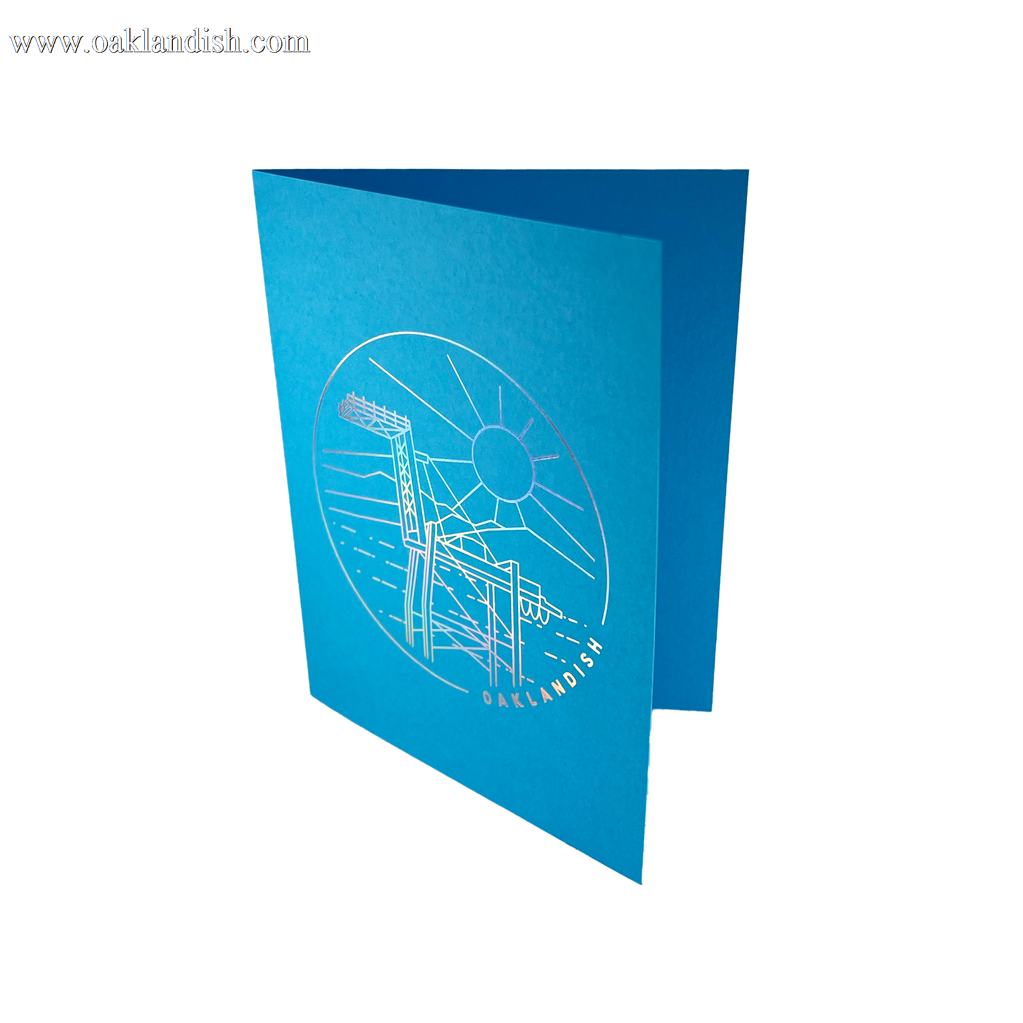Open blue greeting card with a circular gold line drawing of an Oakland crane and OAKLANDISH wordmark.