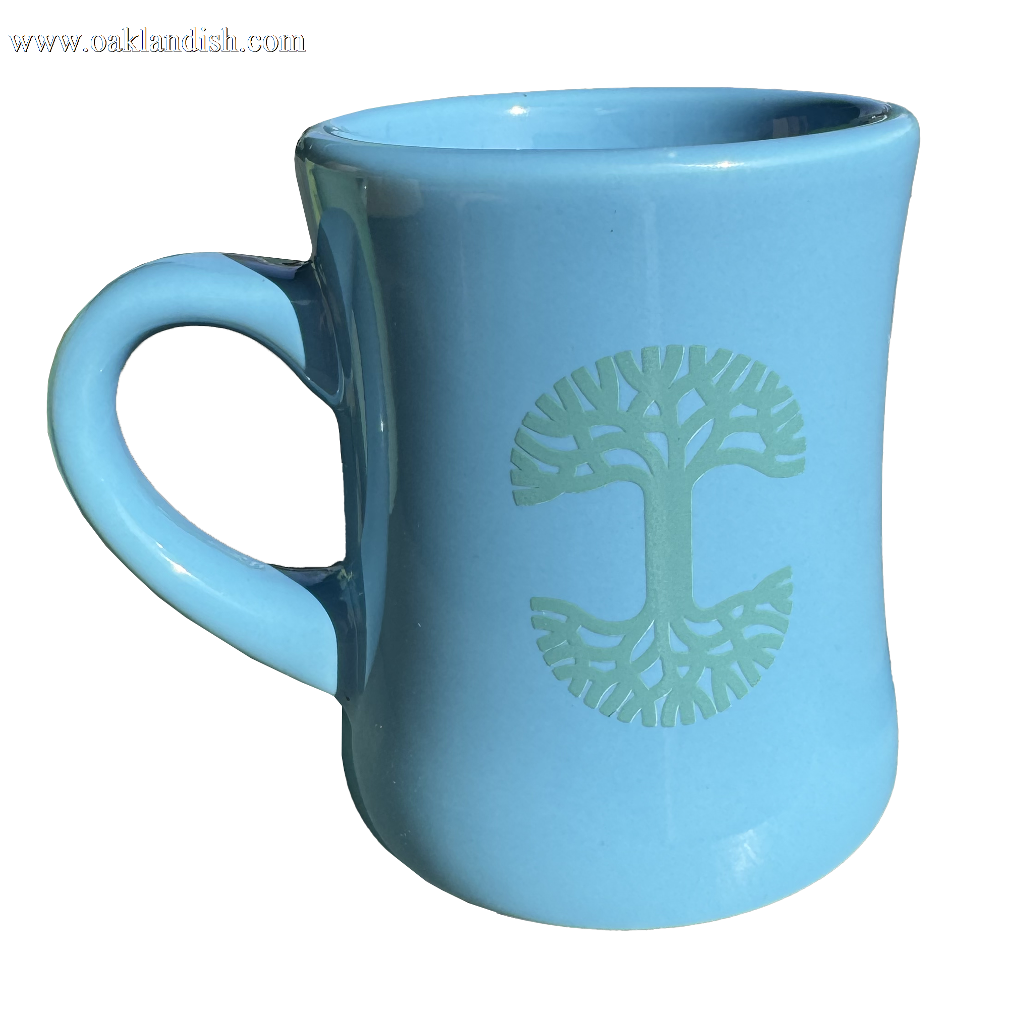 The Oaklandish Diner Mug is a light blue ceramic piece with a wide base and a narrow top, making it ideal for any drinkware collection. It features a green geometric tree design on one side, while the handle takes on a simple half-heart shape, set beautifully against a plain white background.