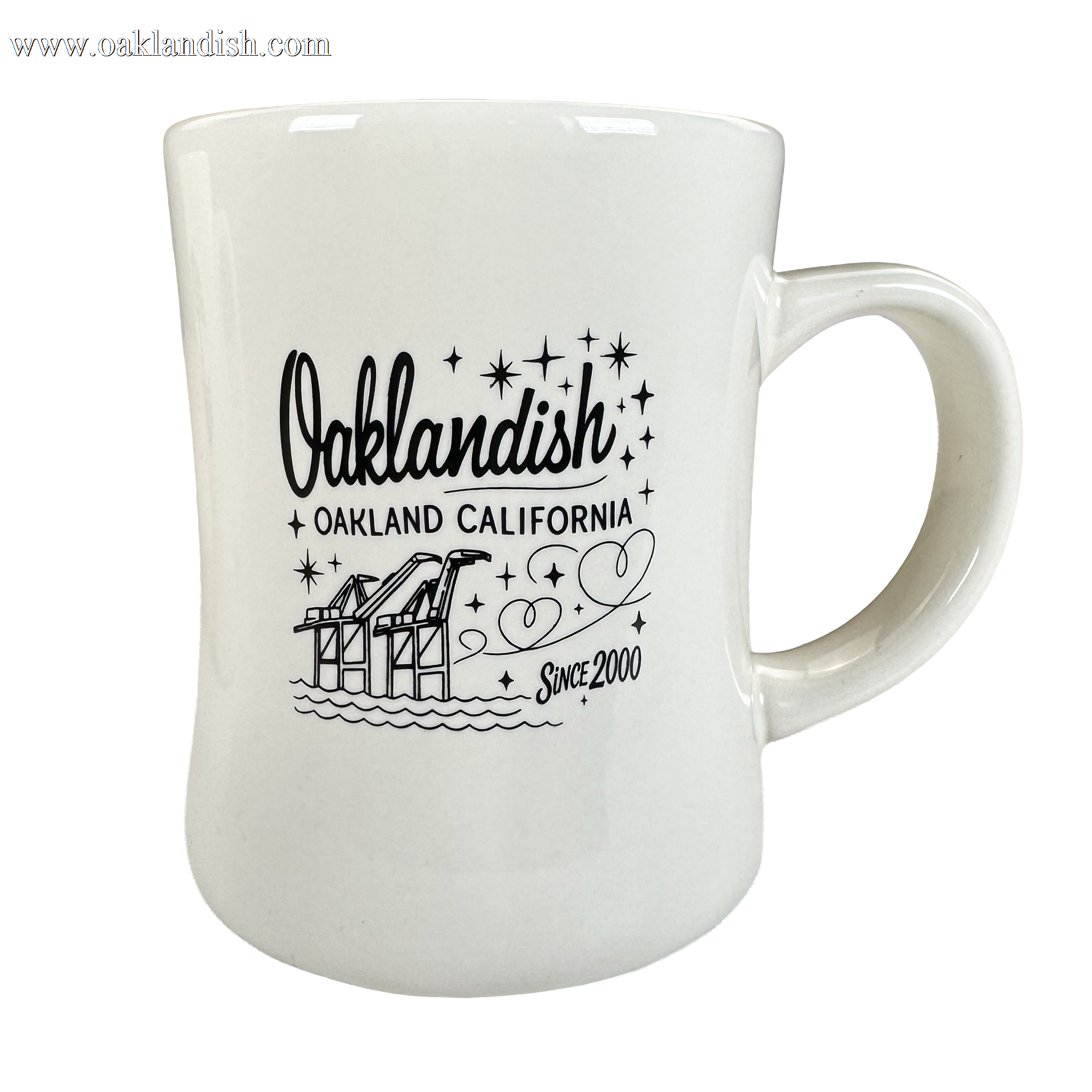 The Oaklandish Cranes Diner Mug is a 14 oz ceramic mug with "Oaklandish Oakland California Since 2000" in black text, illustrated cranes, water, and stars. Its curved design includes a comfy handle and appears against a plain white background.