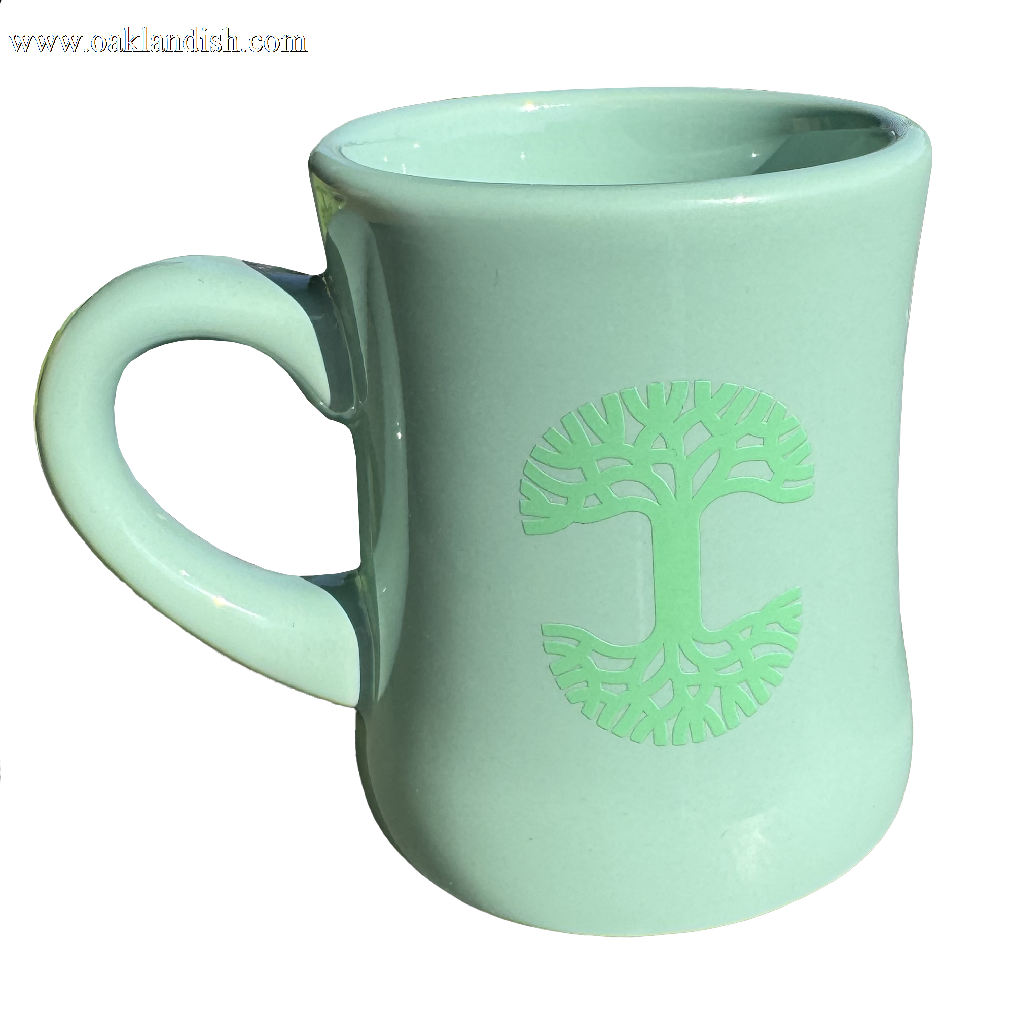 The Oaklandish Diner Mug by Oaklandish is a light green ceramic mug that boasts a stylized tree design embossed on one side. The symmetrical branches and roots of the tree form a circle, adding charm to the drinkware. Its curvy, slightly tapered shape and large handle stand out against a plain white background.