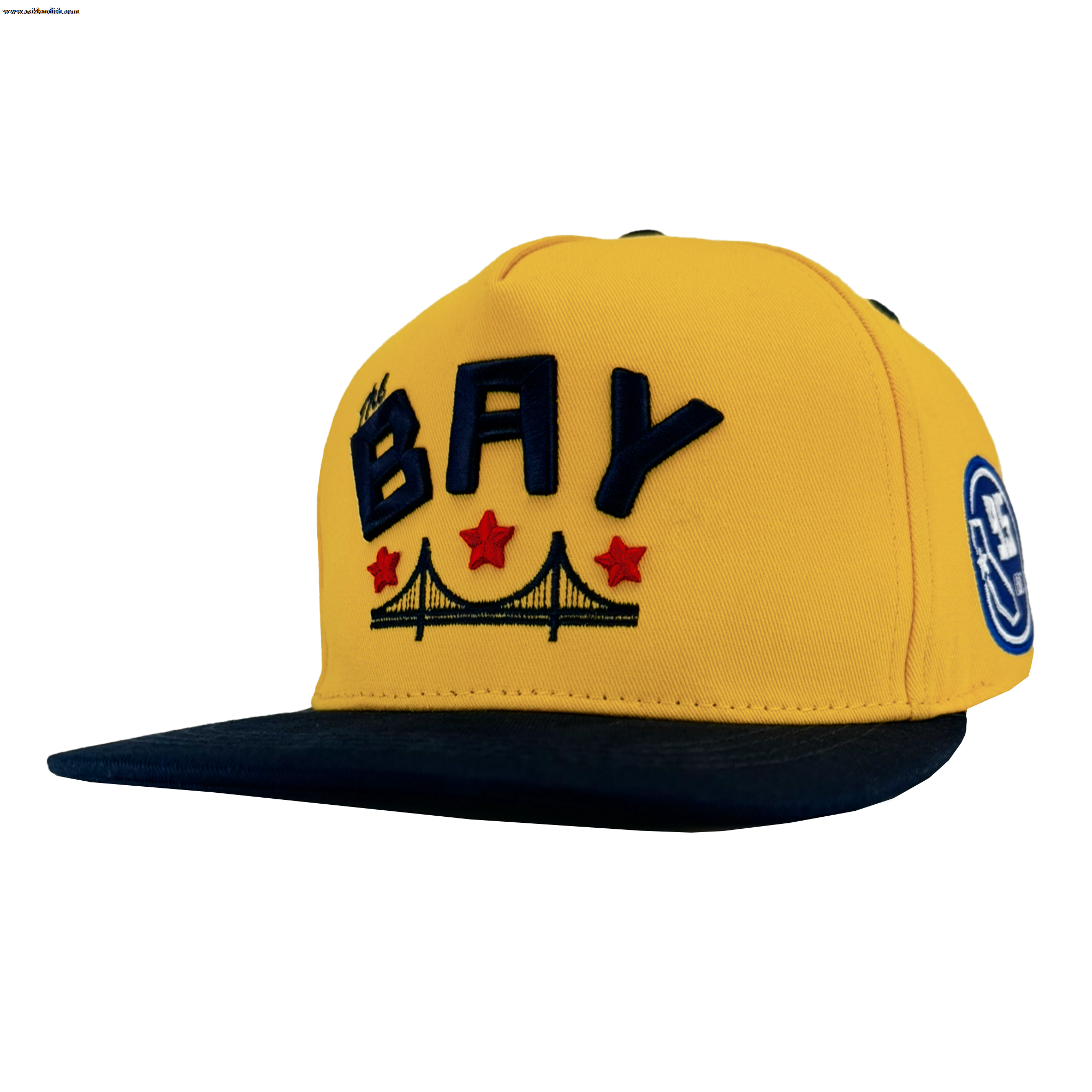 The Bay Bridge Snapback by DOC from Oaklandish is a yellow cap with a dark brim, featuring "BAY" in bold navy letters inspired by Bay Area art and design, a bridge illustration underneath, three red stars above it, and a circular DOC Snapback hat patch on the side.