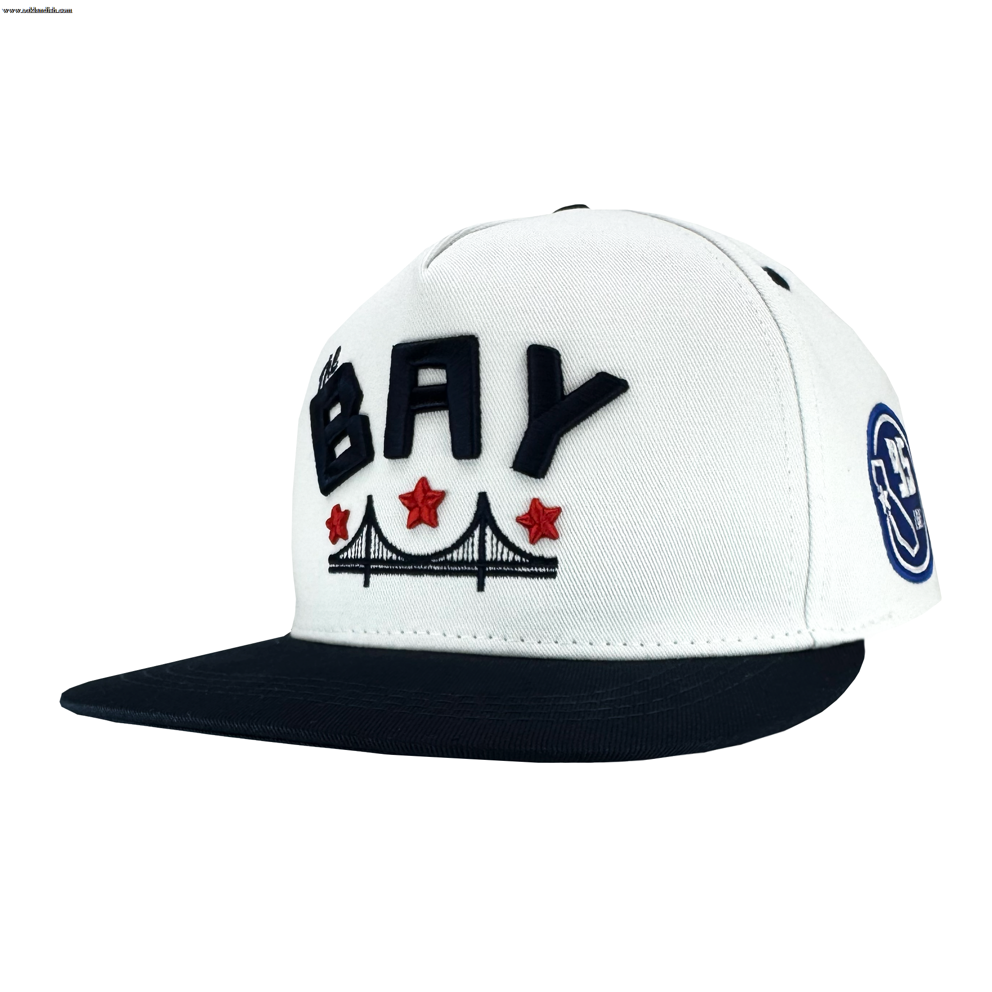The Bay Bridge Snapback by DOC from Oaklandish is a white and black hat featuring "BAY" in bold black letters. It celebrates Bay Area culture with a bridge illustration and three red stars below. The black brim and circular "9FIFTY" logo on the side complete its design.
