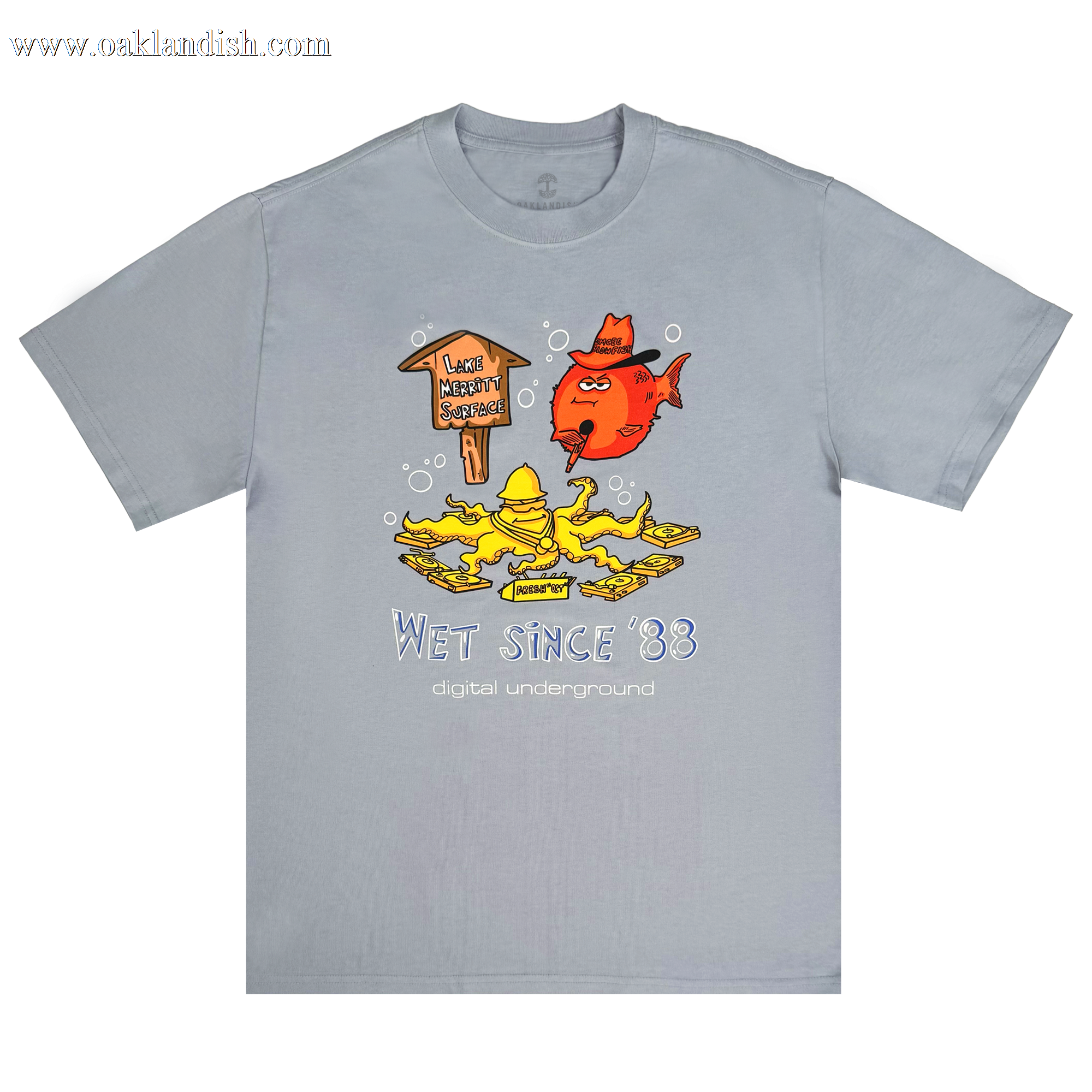 The Oaklandish Wet Since '88 Heavy Tee features a cartoon of a red fish and yellow character underwater near a sign reading "Lake Wabbit Swamp." The text "Wet Since '88" and "Digital Underground" highlights its Oakland roots, with bubbles adding to the aquatic feel.
