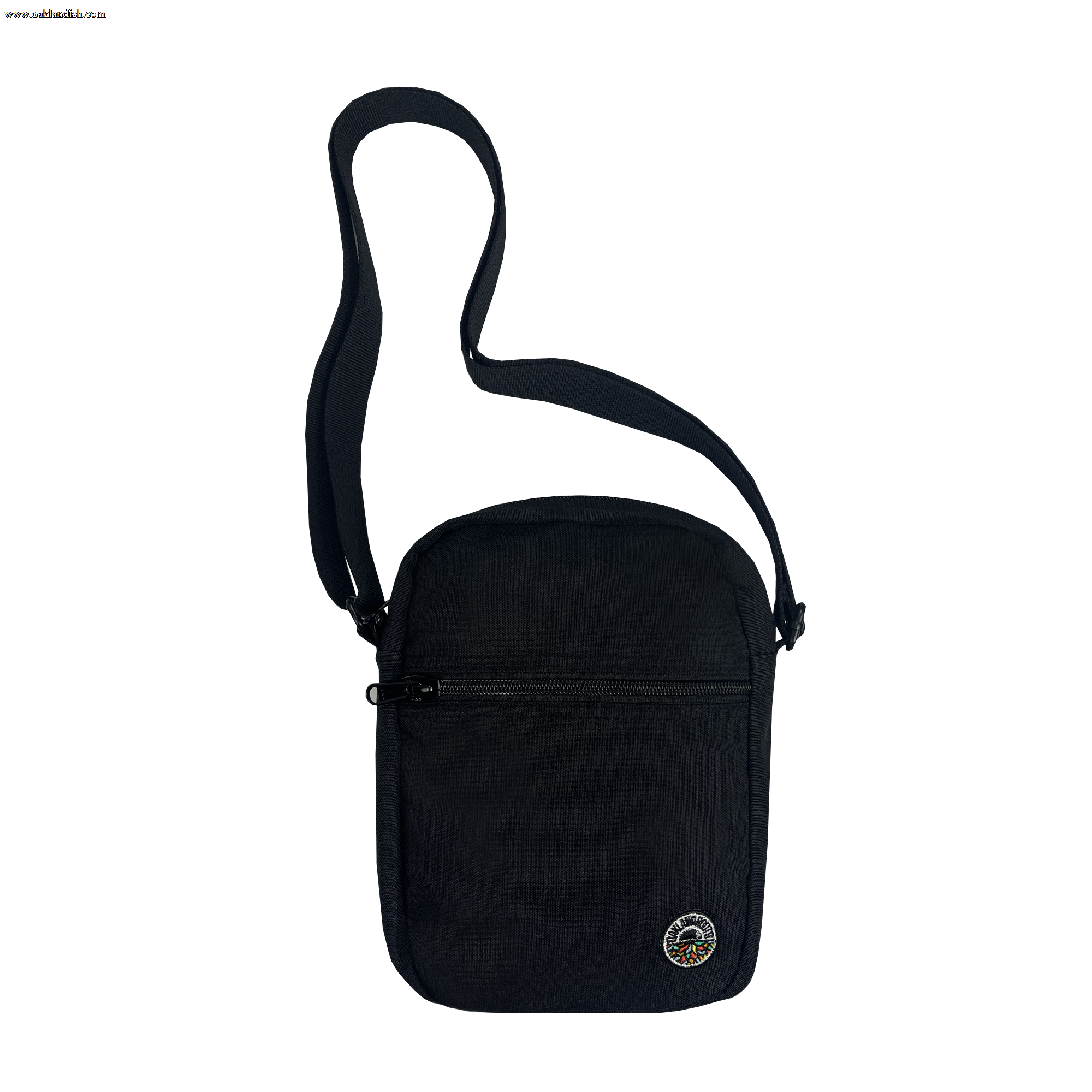 The Oakland Roots SC Flight Bag, a small black shoulder bag from Oakland Roots SC, is showcased. It includes a single adjustable strap and features a zippered front compartment along with a circular patch at the bottom right corner, adorned with colorful designs inspired by the Oakland Roots Sports Club. Made from durable fabric, this bag is ideal for everyday use.