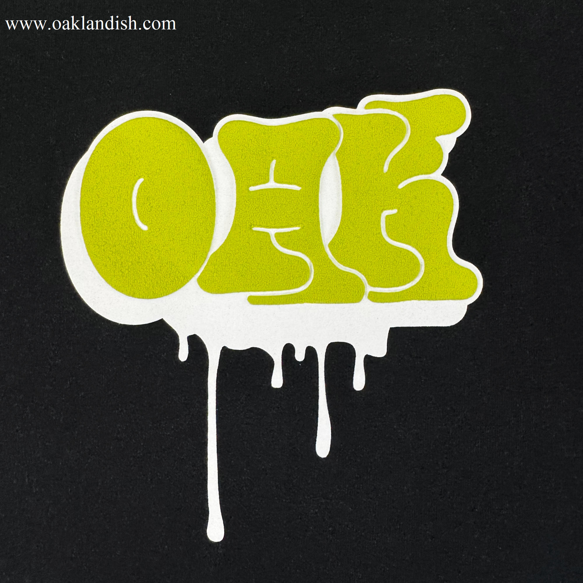 The Oaklandish Graff OAK Tee features "OAK" in bold, bright green graffiti letters with a dripping white outline on a solid black, 100% cotton classic fit.