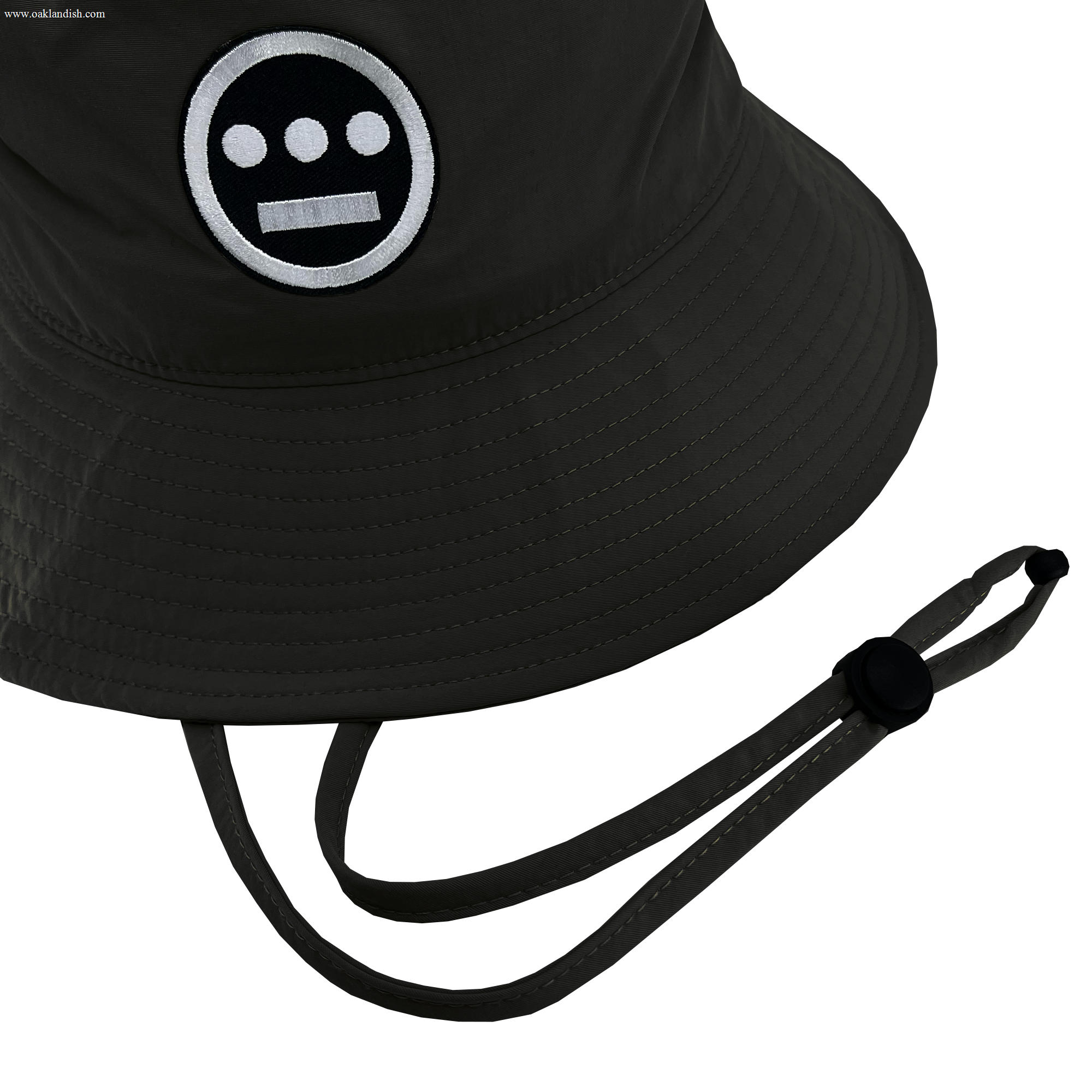 The Hiero Boonie Hat by Hieroglyphics is a dark-colored bucket hat crafted from recycled nylon, featuring a logo with a circular face, two white eyes, and a horizontal bar for a mouth. It includes a chin strap with an adjustable toggle, and the stitching and texture of the fabric are visible.