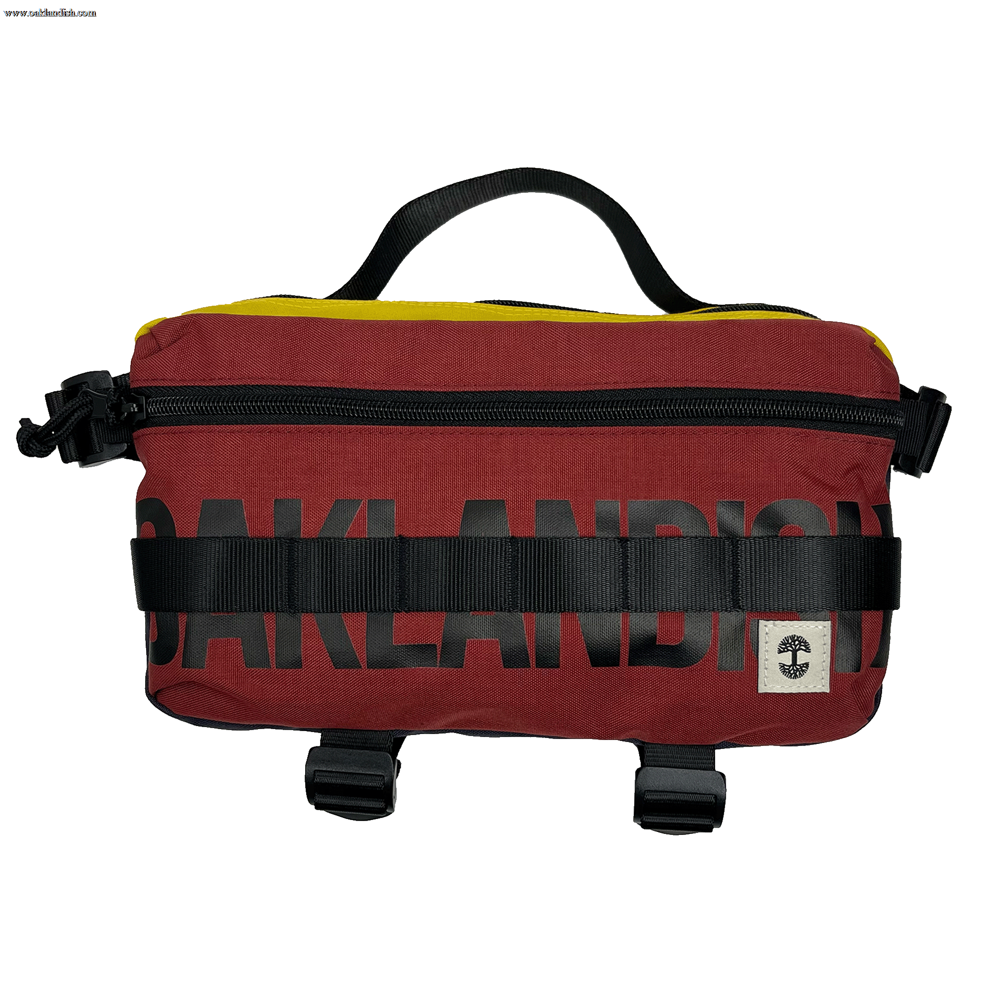 The Oaklandish Hip Bag is a rectangular, maroon waist bag featuring black zipper and buckle details for a premium look. The word "OAKLANDISH" is prominently displayed in black block letters across the front. A small white label with a black tree logo decorates the lower right corner, and a black handle on top adds to its unisex appeal.