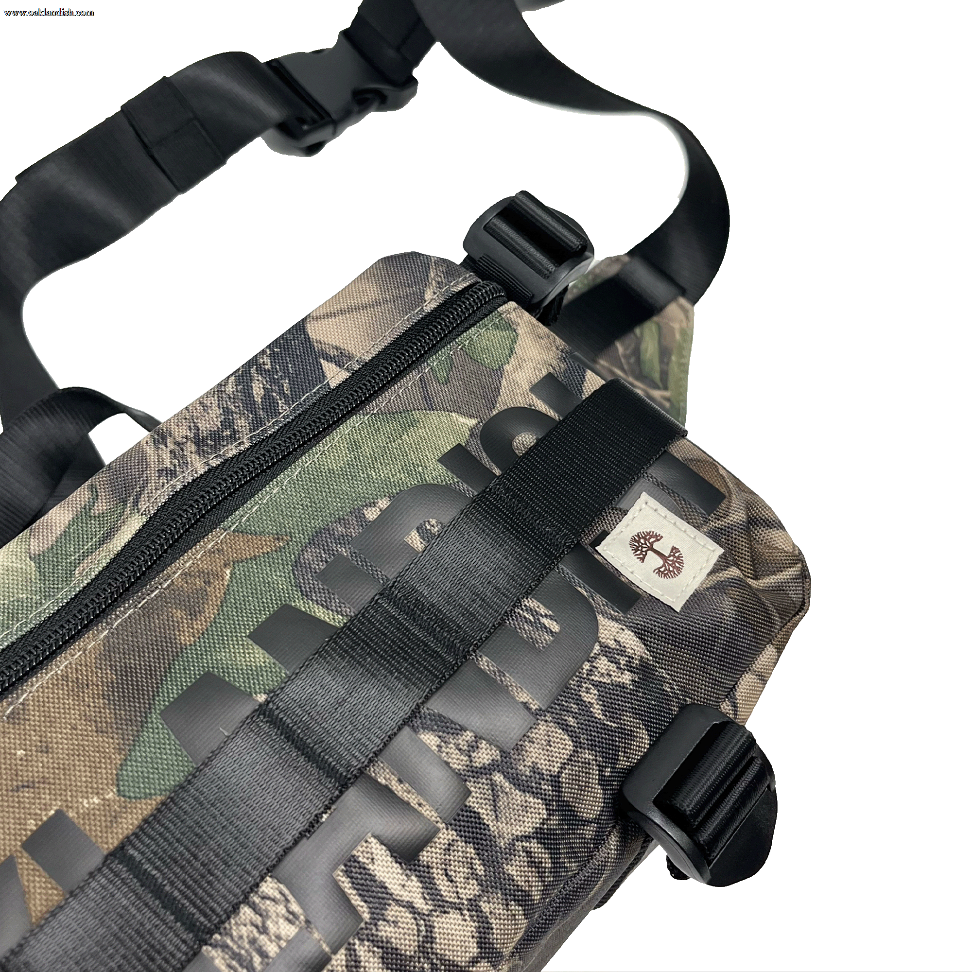 Top side view of a camo pattern cross-body bag with front zipper and large black Oakladish wordmark and Oaklandish tree logo patch.