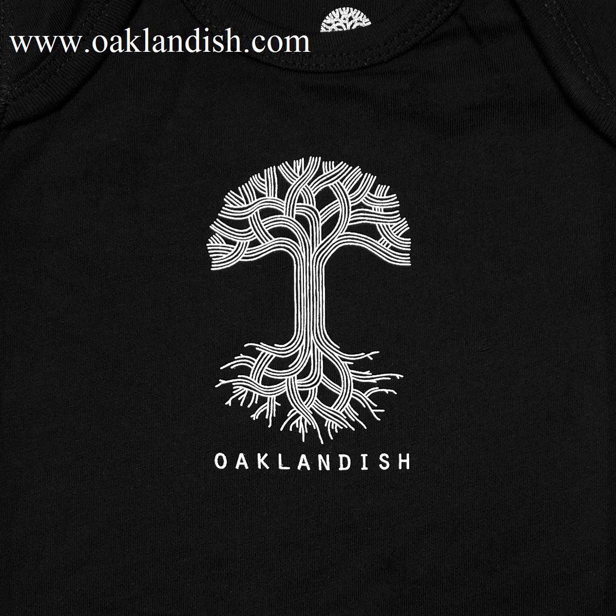 The Infant Oaklandish Classic Logo One-Piece by Oaklandish is a black romper made from 100% cotton. It features a detailed white graphic design of a tree with intricate, interwoven branches and roots, along with reinforced snap closures for added durability. Below the tree, "OAKLANDISH" is printed in bold white uppercase letters.