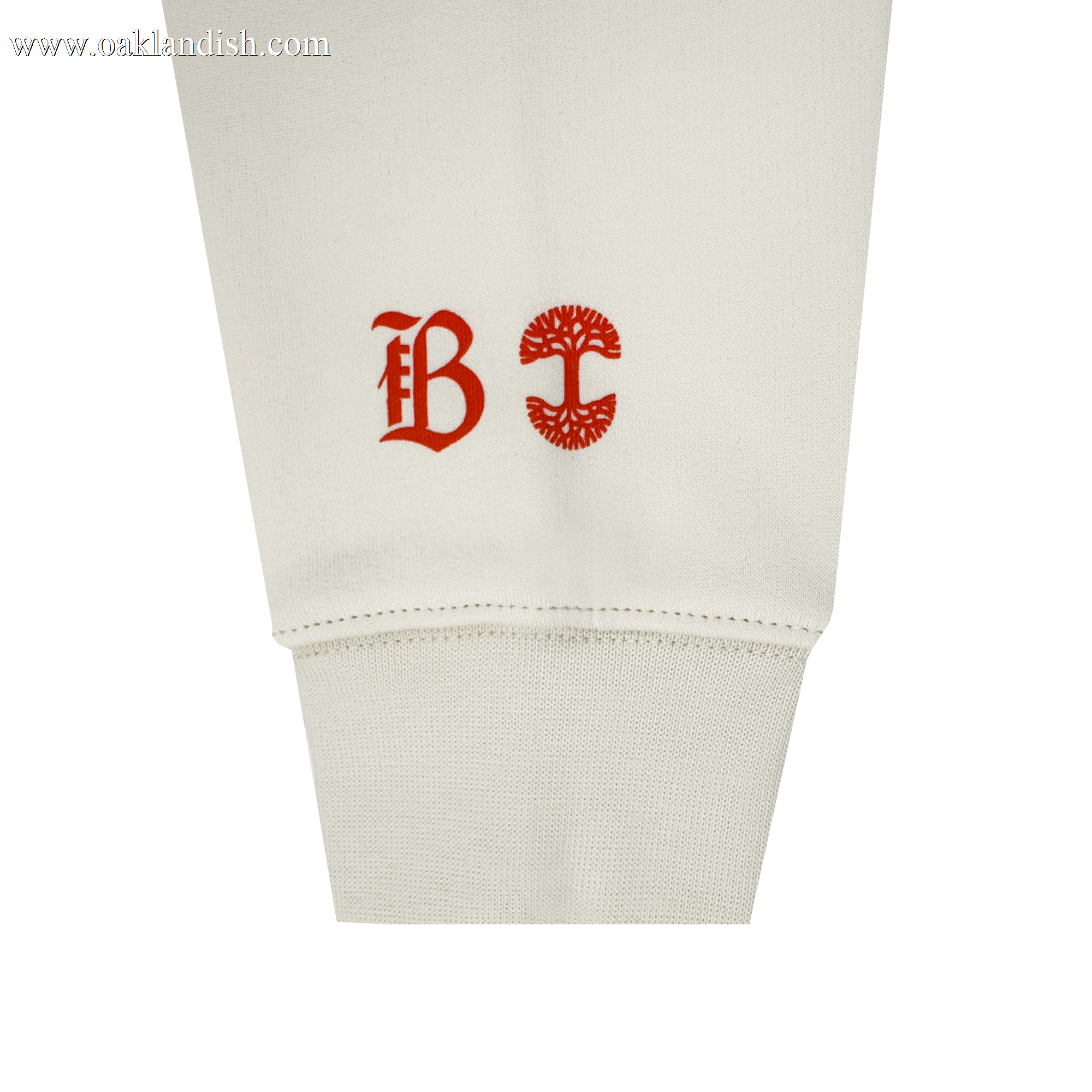 A close-up of the Bay FC Jubilee Crew shows its off-white cuff and sleeve, featuring two red symbols: Bay FC’s stylized “B” logo and a circular tree emblem, printed side by side above the cuff.