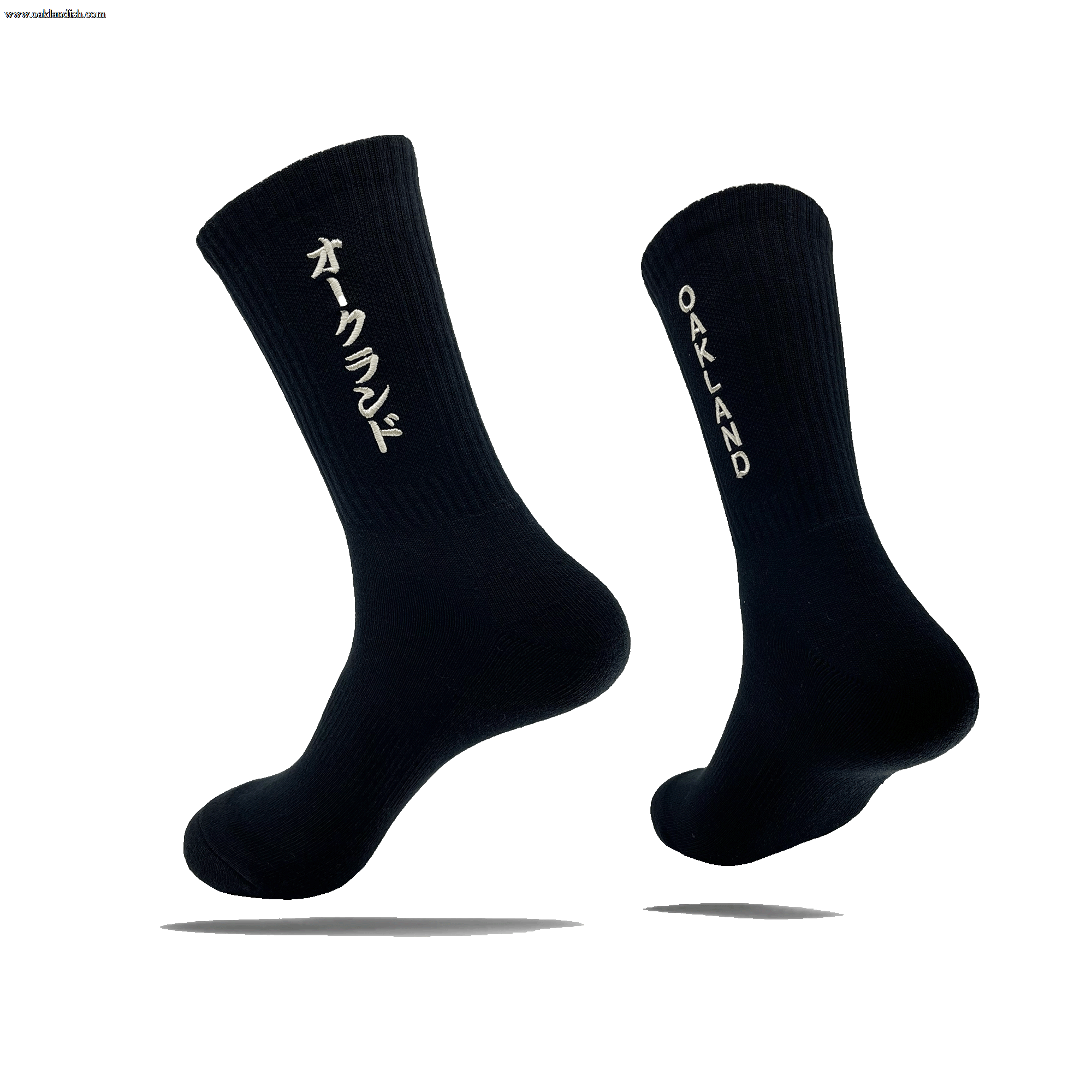 Side view of a pair of black crew socks with OAKLAND wordmark on the side of one sock and Kanji Japanese writing on the other.