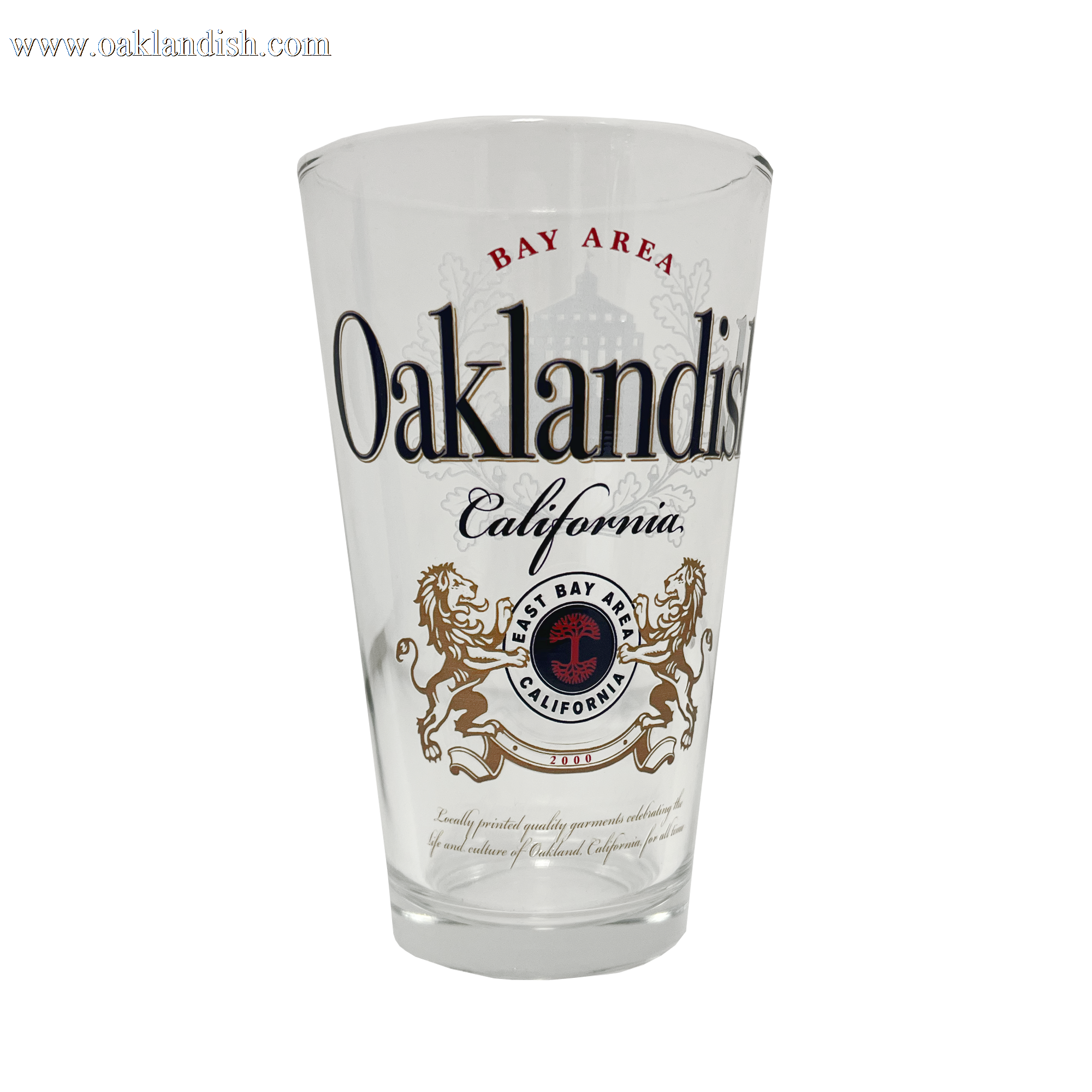 The Lager Pint Glass by Oaklandish is a 16 oz pint glass featuring the text "Bay Area Oaklandish California" in black and red. Below this, intricate graphics depict two lions standing on their hind legs, flanking a red and black emblem that reads "East Bay" and "California." Additional small text appears beneath the emblem, making it perfect for any drinkware collection.