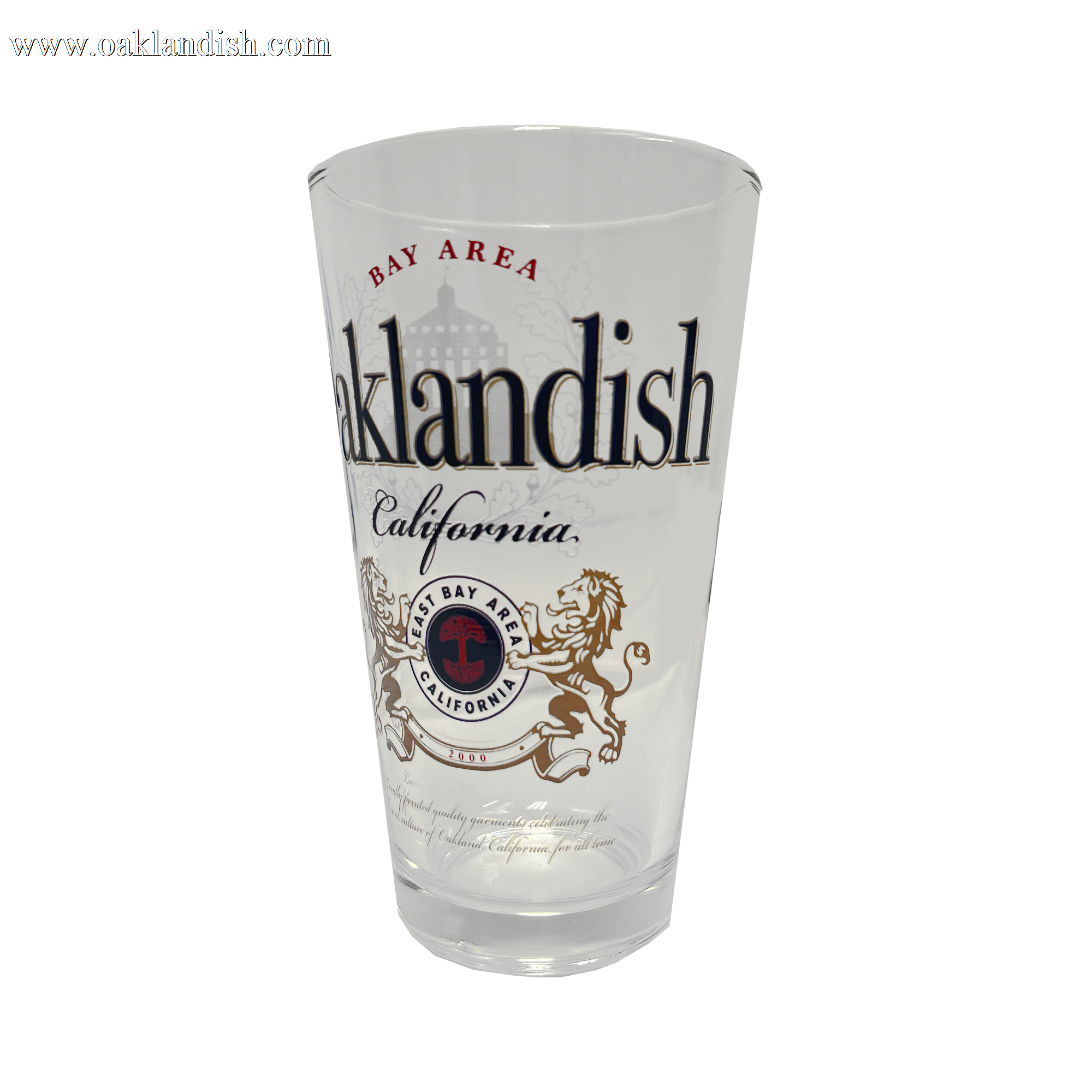The **Lager Pint Glass** by **Oaklandish** is a stylish 16 oz pint glass featuring "Oaklandish" and "California" in bold black text. Above "Oaklandish," "Bay Area" is written in red, while below, a circular emblem displays "Bay Area California" flanked by two lions. The background of this practical drinkware is white, combining local pride with everyday functionality.