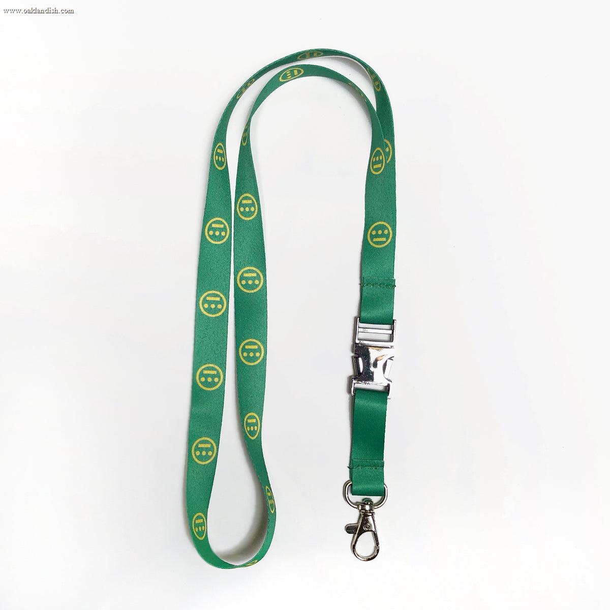 The Hieroglyphics Hiero VIP Lanyard features a vibrant green design adorned with yellow smiley face patterns. It comes equipped with a silver clasp and buckle, as well as a metal swivel hook for easy attachment of your key chain. The plain white background highlights the lanyard’s striking appearance.