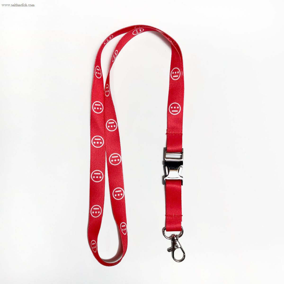 The Hieroglyphics Hiero VIP Lanyard features a red design with a repeating pattern of white smiley faces. It includes a black plastic quick-release buckle in the middle and a metal swivel hook at the end, perfect for attaching items like keys or ID cards. Ideal for organizing your key chain, it is showcased laid flat against a plain white background.