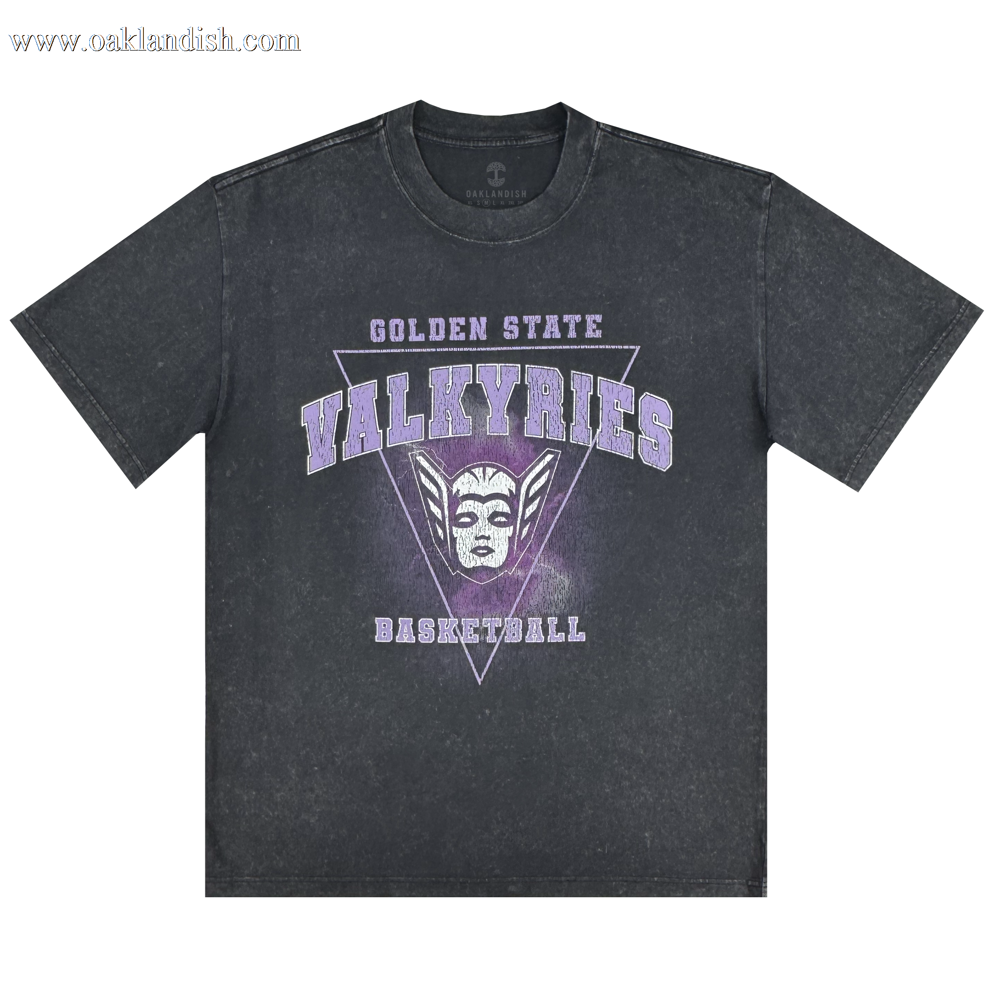 The GSV Golden State Valkyries Surge Stone Wash Heavy Tee is a black acid-wash shirt with "Golden State Valkyries Basketball" in white and purple, a stylized Valkyrie mask and purple triangle on the front. Made from soft organic cotton, with short sleeves and a relaxed fit.