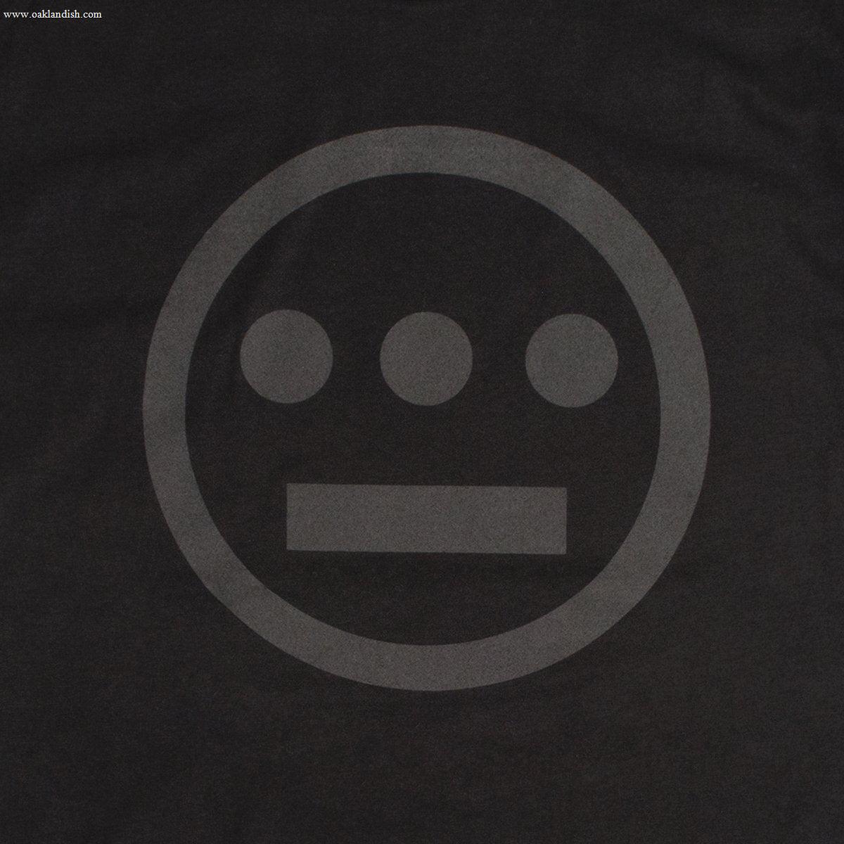 The Hiero Classic Logo Tee by Hieroglyphics features a minimalist grayscale design on a black background. The design consists of three small filled circles lined horizontally above a short, thick horizontal bar, all enclosed within a larger circle. The elements resemble modern hieroglyphics subtly shaded against the dark backdrop, making it perfect for a t-shirt.
