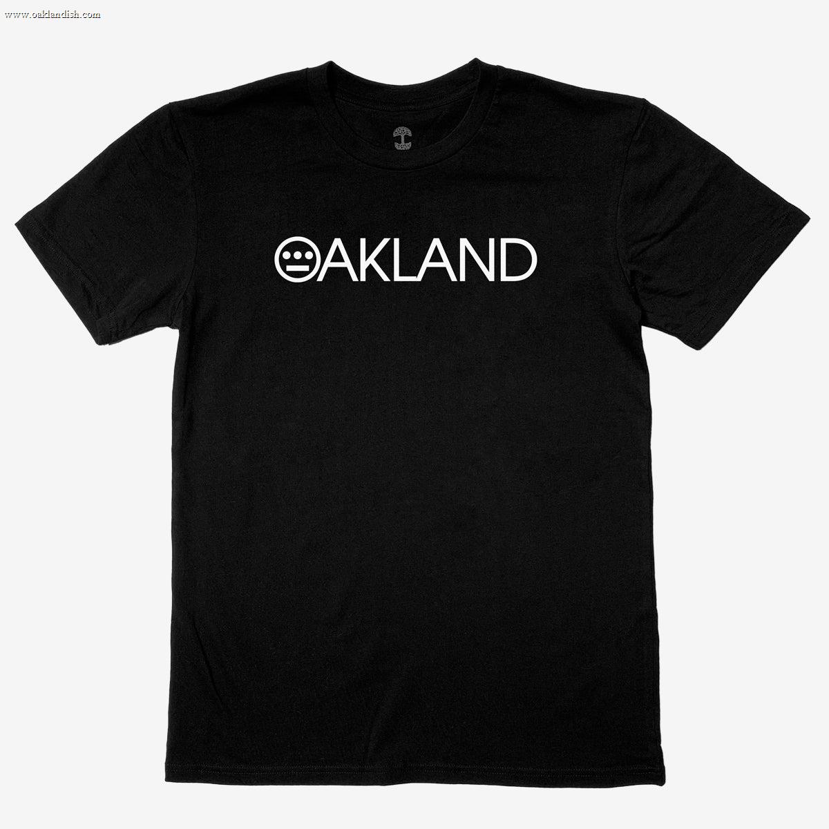 The Hieroakland Tee by Hieroglyphics is a black, 100% cotton T-shirt featuring the word "OAKLAND" in white capital letters across the chest. The "O" is uniquely stylized with a smiley face made of three horizontal lines within the circle. With its classic fit, simple crew neck, and short sleeves, this shirt is perfect for promoting Town business. It's displayed against a plain white background.