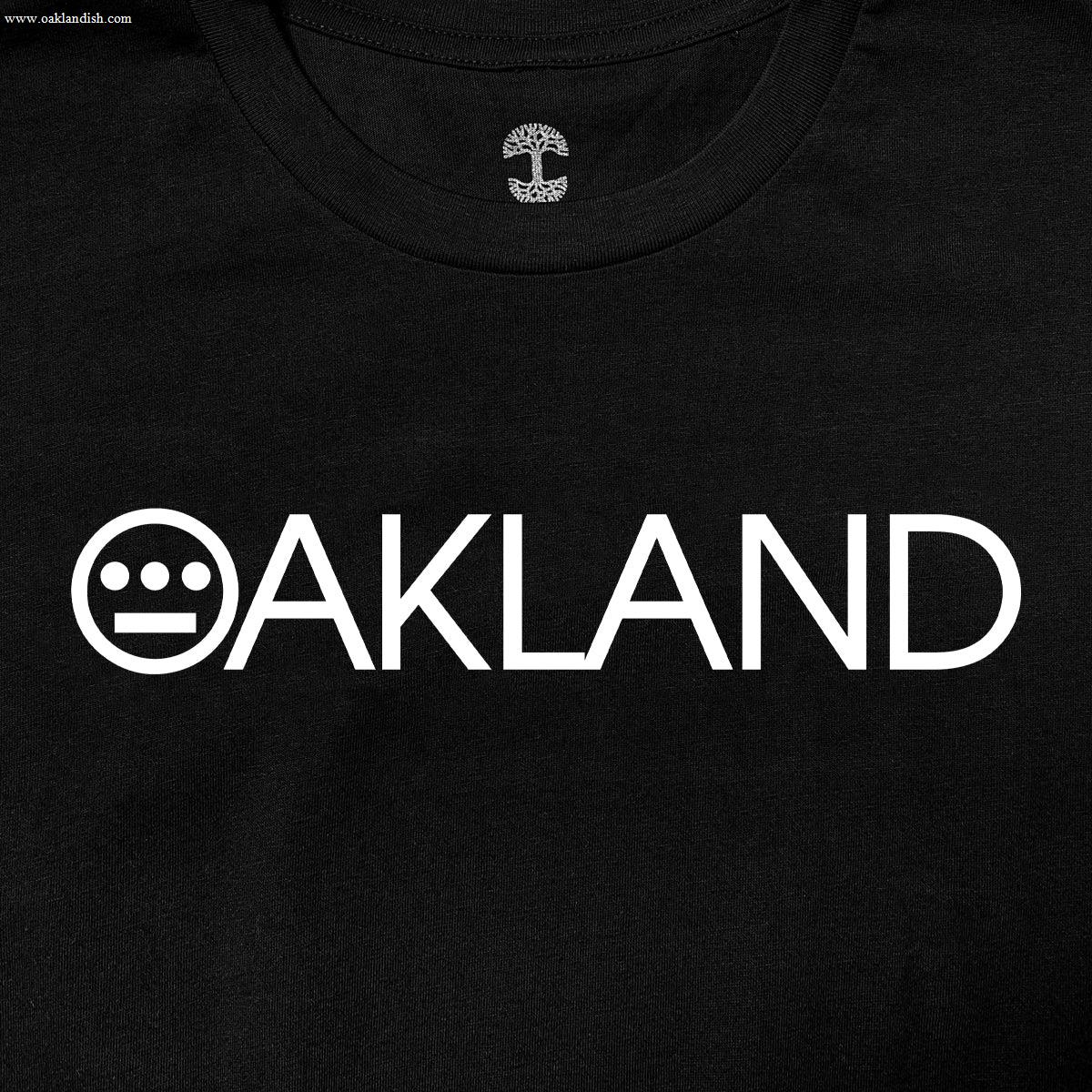 The Hieroakland Tee by Hieroglyphics is a black, 100% cotton T-shirt featuring the word "OAKLAND" in bold, white capital letters across the chest. The "O" is uniquely stylized with three horizontal dots above two vertical lines. Inside the neckline area, there's an intricate tree design that adds a special touch to this classic fit T-shirt, making it perfect for any town business.