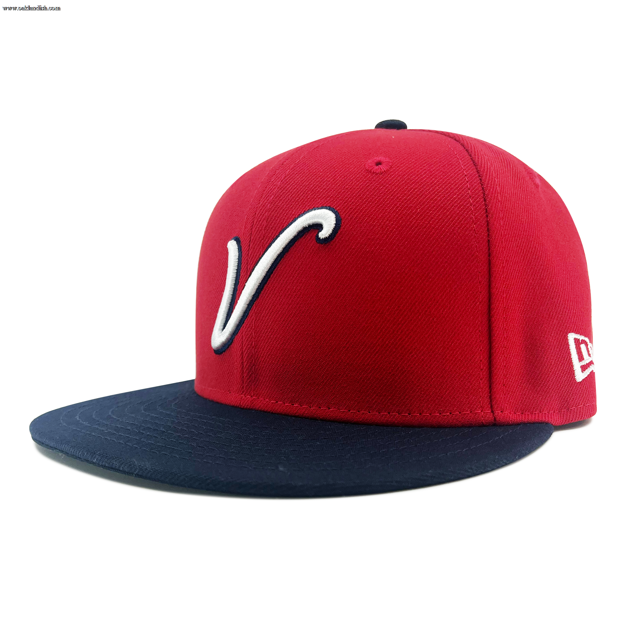 A red New Era El Aguila Alt 59FIFTY Cap featuring a navy blue flat brim. The front showcases a large, white, stylized “V” outlined in navy, while the white New Era logo is embroidered on the side. This fitted cap is displayed against a plain white background.