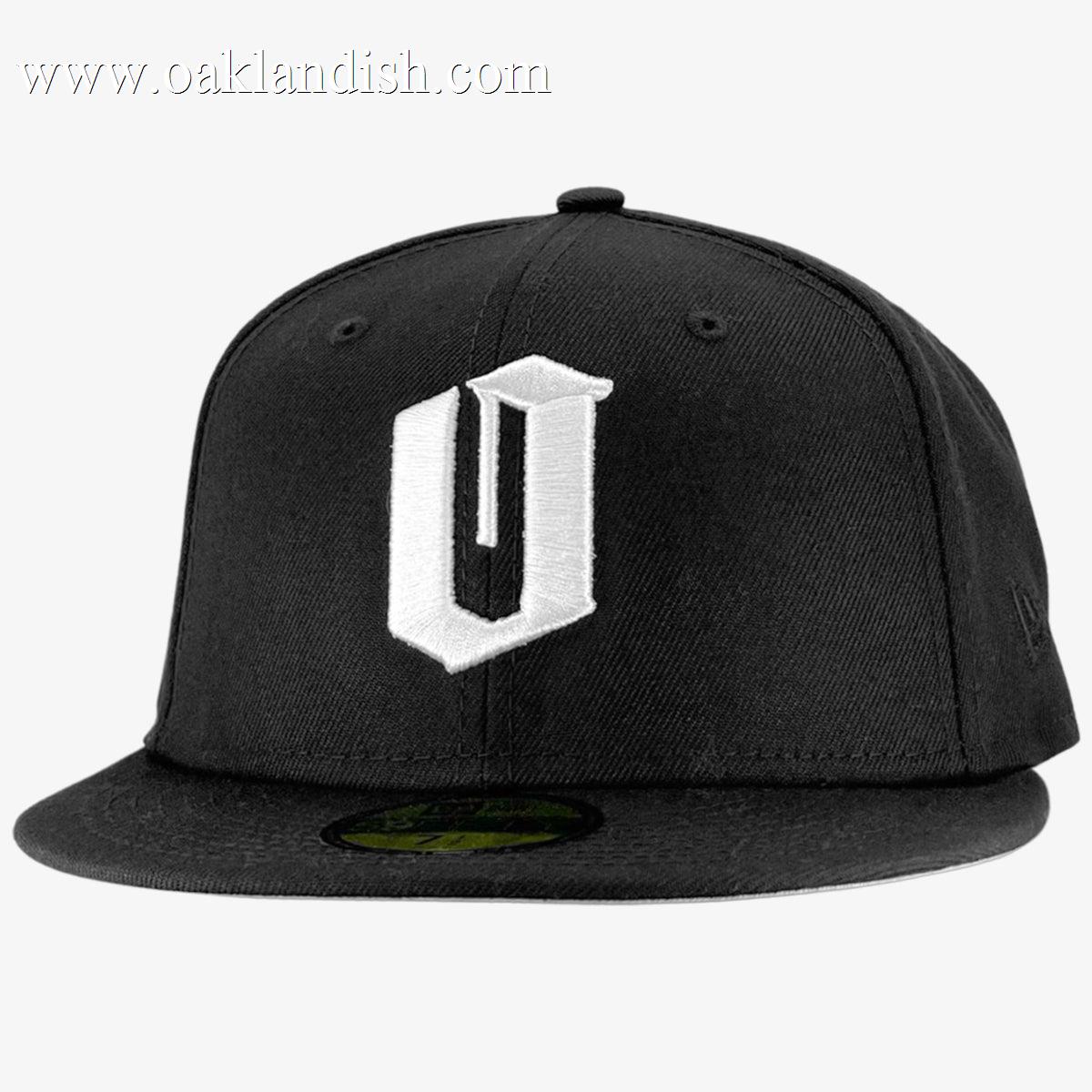 A black New Era Official 59FIFTY Fitted Cap featuring a prominent white embroidered “U” on the front. The structured crown and signature round sticker emphasize its authenticity, while a plain light gray background brings focus to the Oaklandish-inspired design. Brand: Other.