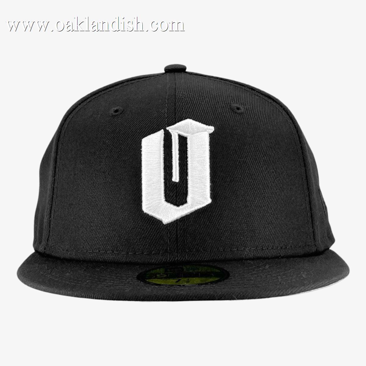A black New Era Official 59FIFTY Fitted Cap by Other showcases a prominent, stylized white “U” embroidered on the front panel. The cap includes a round button at the crown and features the iconic 59FIFTY sticker on its flat brim. Set against a plain white background, the image highlights the cap’s unique design and detailing.