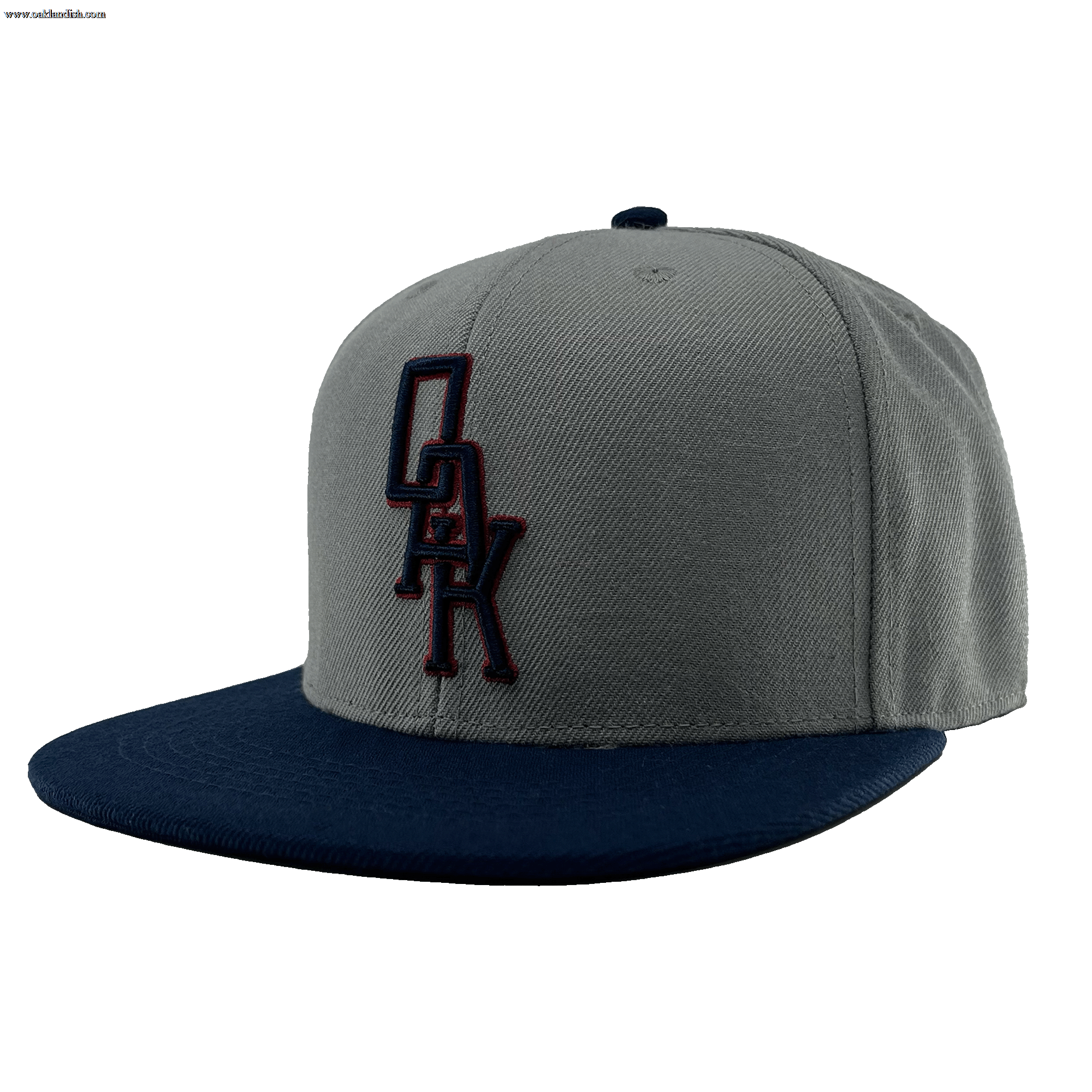 The OAK Monogram Snapback by Oaklandish features a gray crown with a flat, navy blue brim. An embroidered black OAK logo with a red outline adorns the front, and the top button matches in navy blue. Displayed from a front-angled perspective, this hat stylishly celebrates Oaklandish pride.