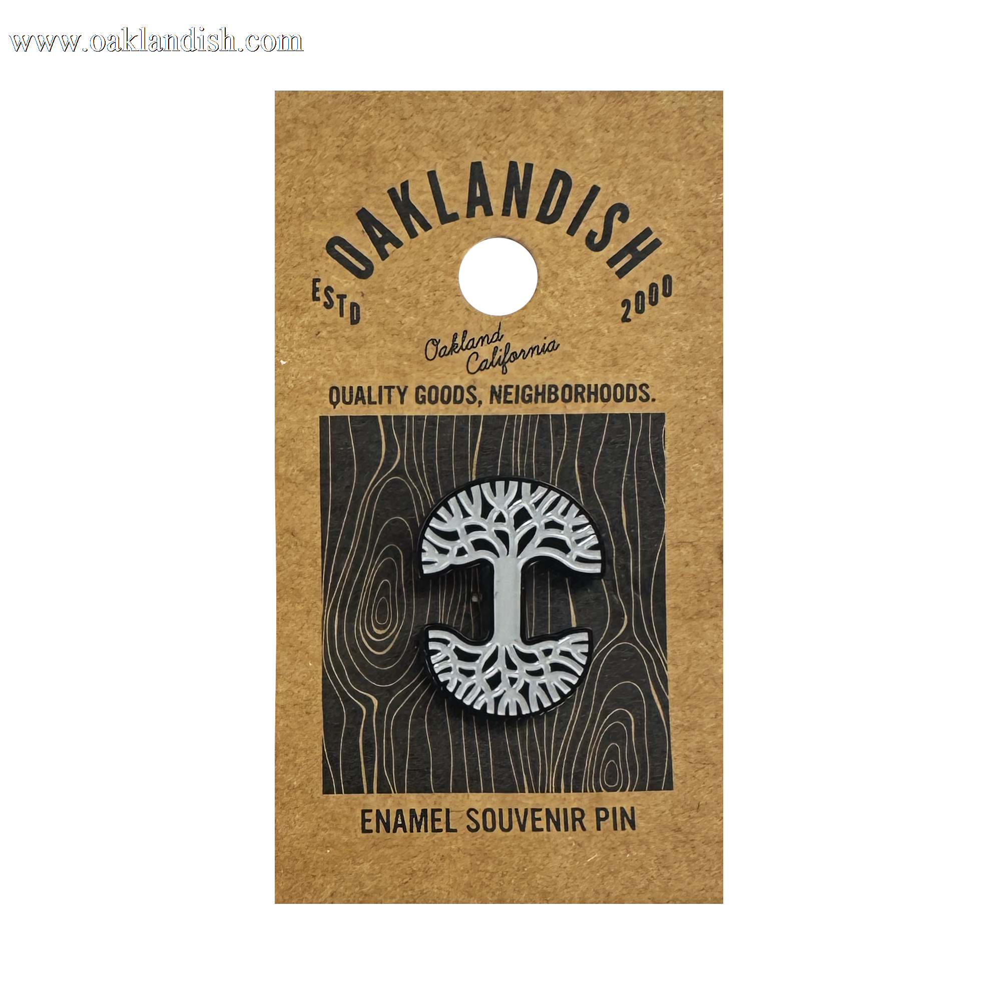 The Oaklandish Logo Enamel Pin by Oaklandish features a black and white enamel abstract tree on a brown kraft card reading "OAKLANDISH ESTD 2000, Oakland California, Quality Goods, Neighborhoods" with a grey woodgrain background.