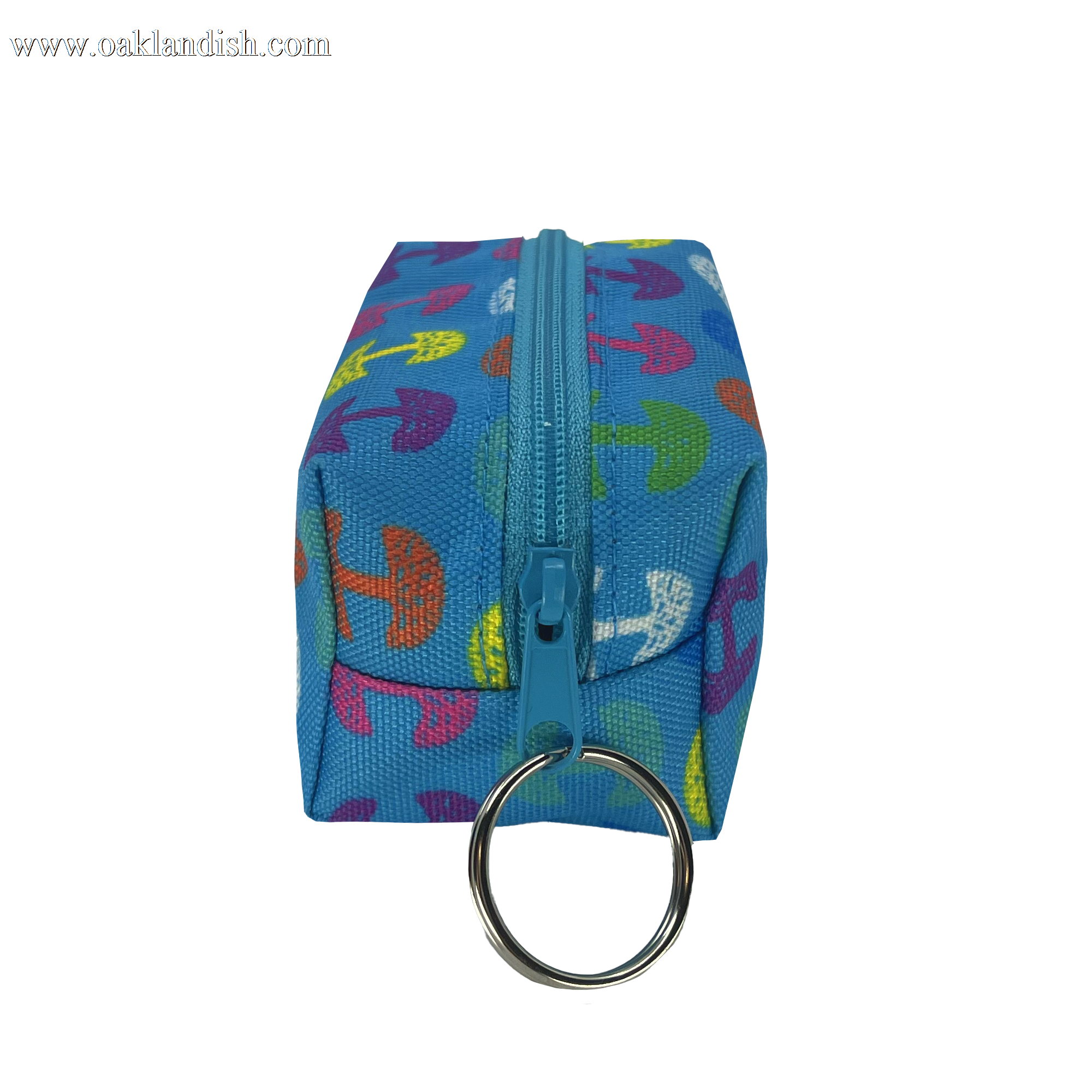 The Oaklandish Repeat Tree Mini Dopp by Oaklandish is a small, rectangular blue fabric pouch with a turquoise zipper running along the top. This mini keychain pouch features vibrant, multicolored umbrella patterns and has a silver keyring attached to one end of the zippered compartment.